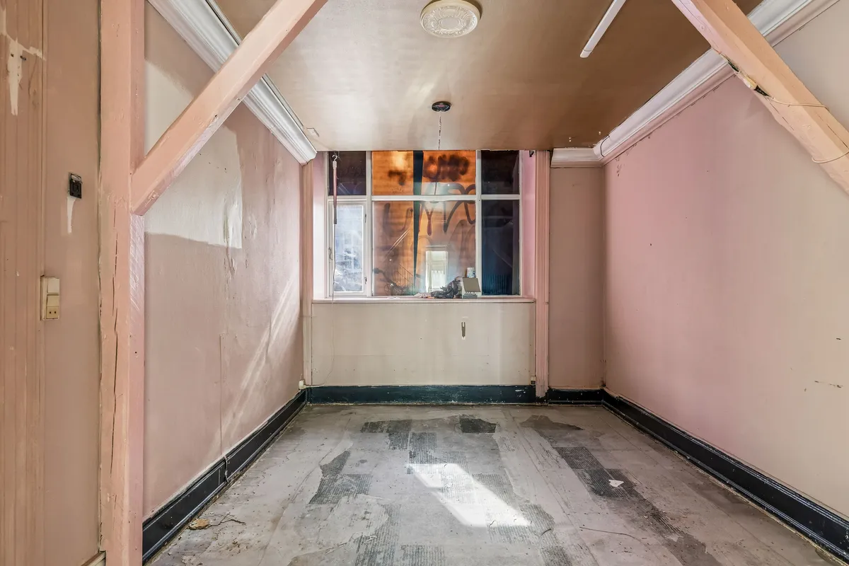 Værelse med lys og tagbjælke. Trægulv og lyserøde vægge. Vindue med graffiti og udsigt til gaden.