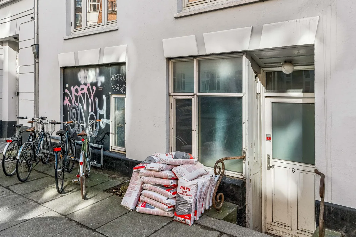 En hvid bygning med flere cykler parkeret og flere poser med Mira cement foran døren.