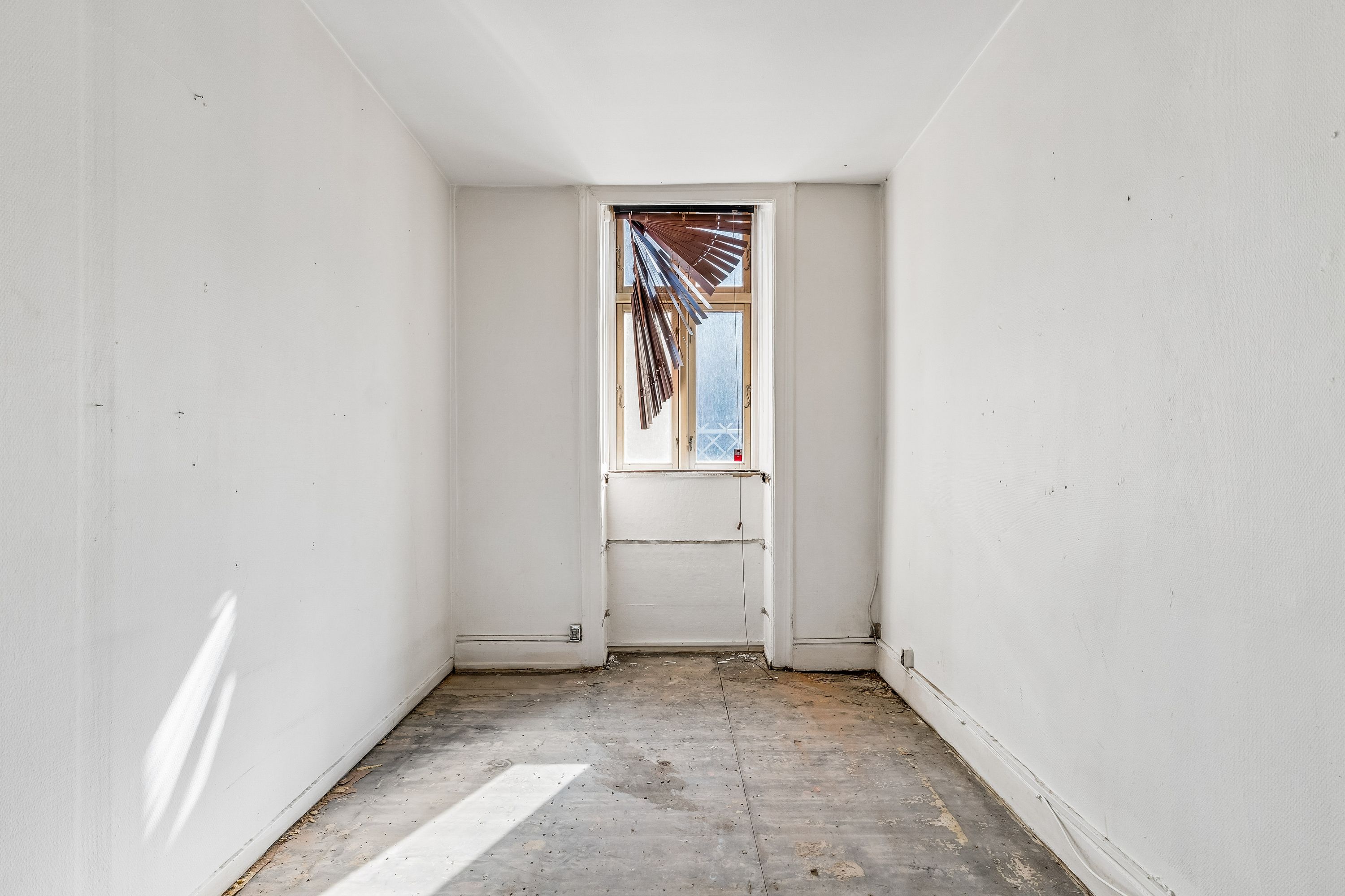 En tom, hvidrums lejlighed med en træruderet vinduesåbning og et gulv med snavs og snavs.