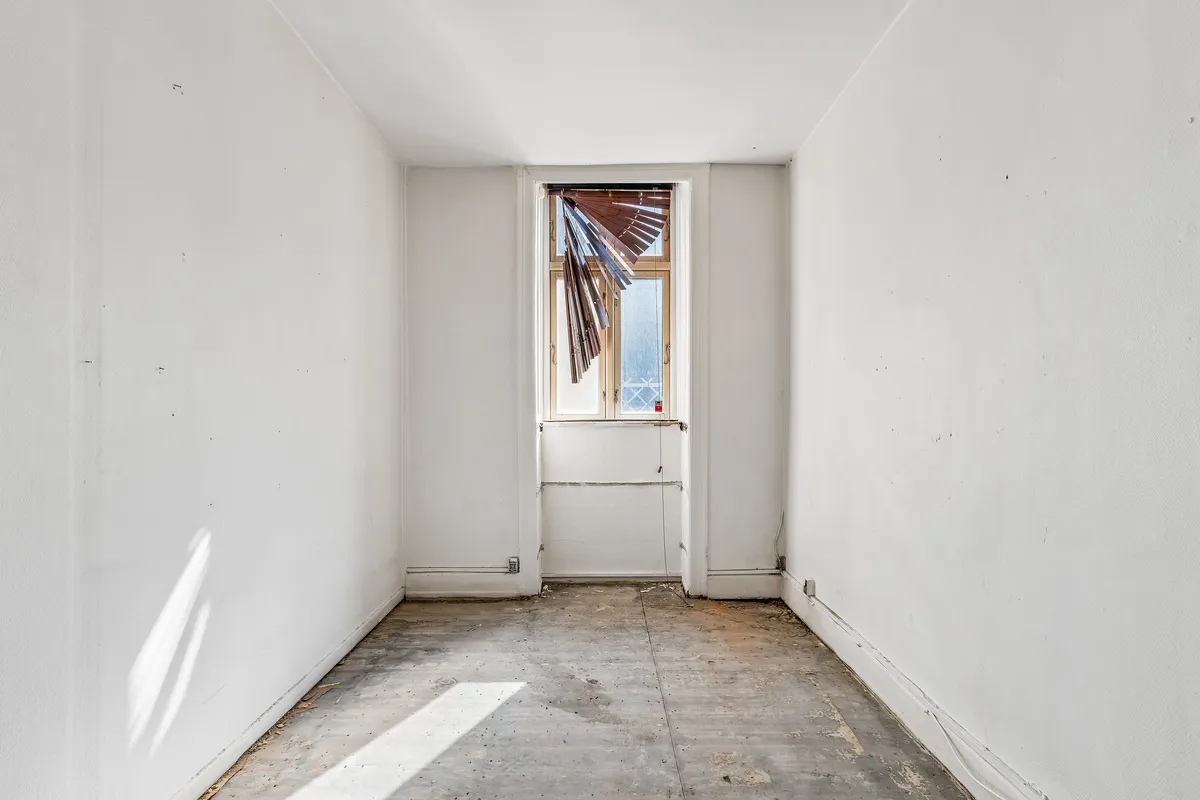 En tom, hvidrums lejlighed med en træruderet vinduesåbning og et gulv med snavs og snavs.