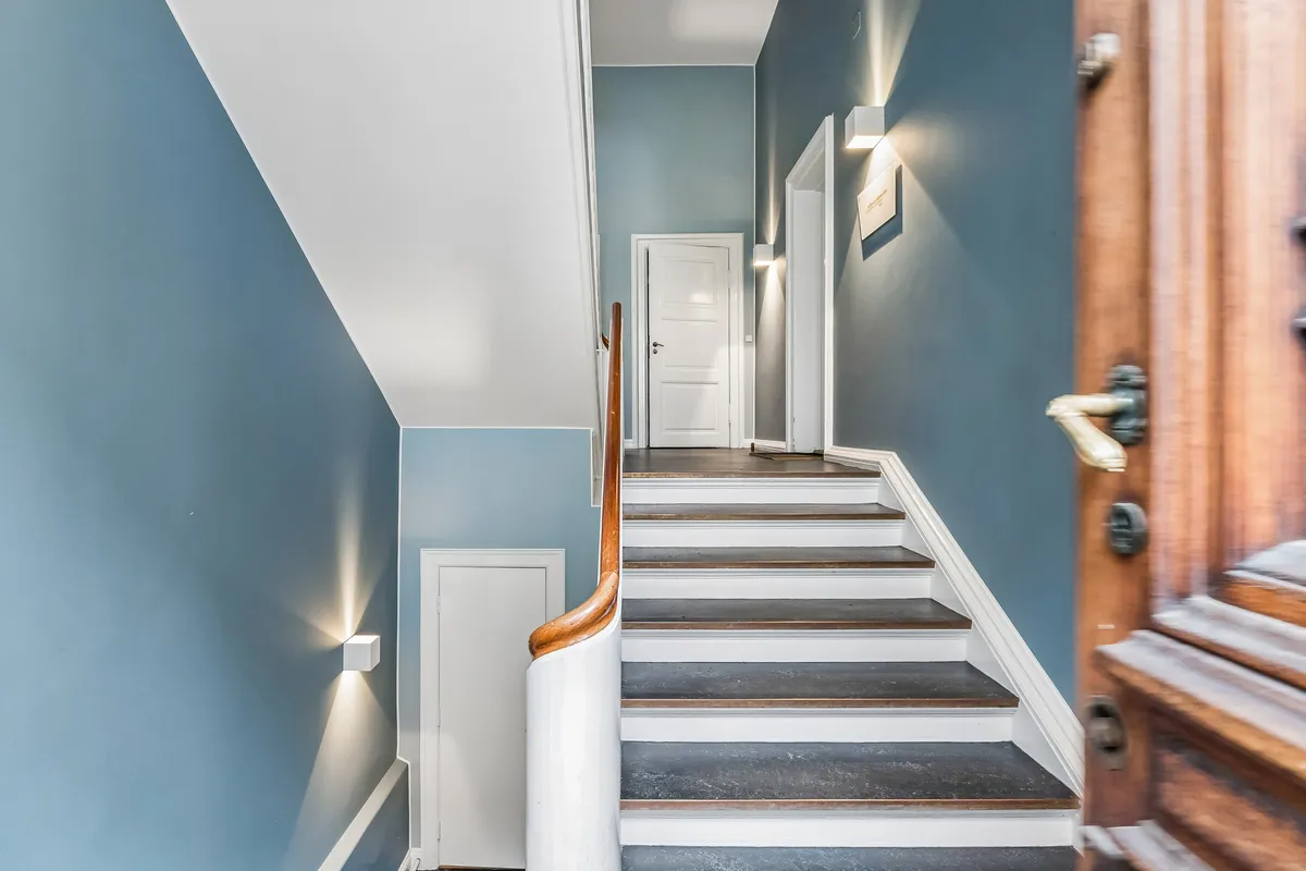 Kontor med to store rum og trappe med hvid og brun farve, der fører til to hvide døre og lysekroner på væggen