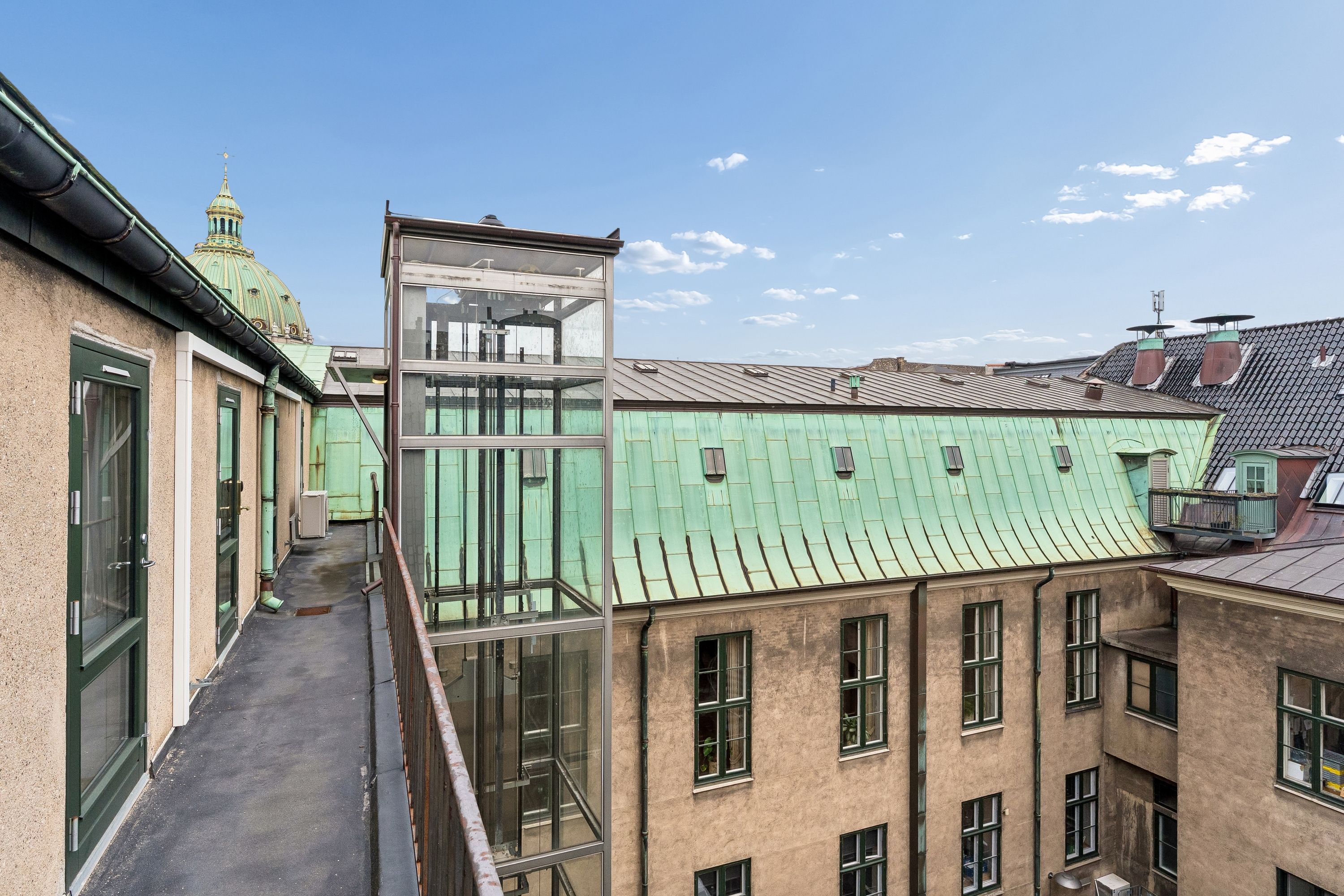 En stor bygning med glasdækket elevator på taget og mange vinduer og røgkammer på taget