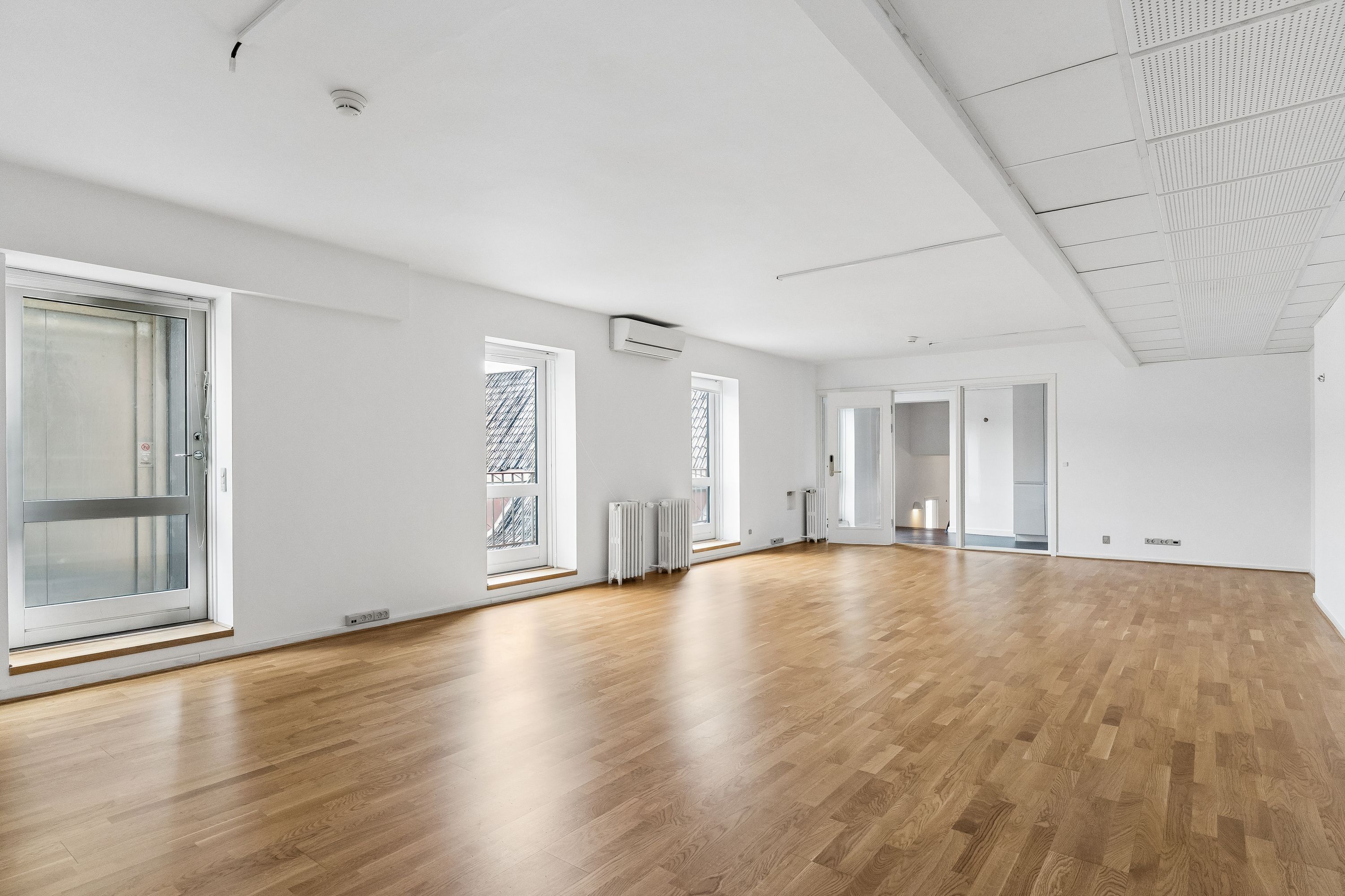 Rummelig lejlighed med lyse gulvbelægning, store vinduer og lysetak, klimaanlæg og radiatorer samt døre og vinduer med hvidt rammeværk