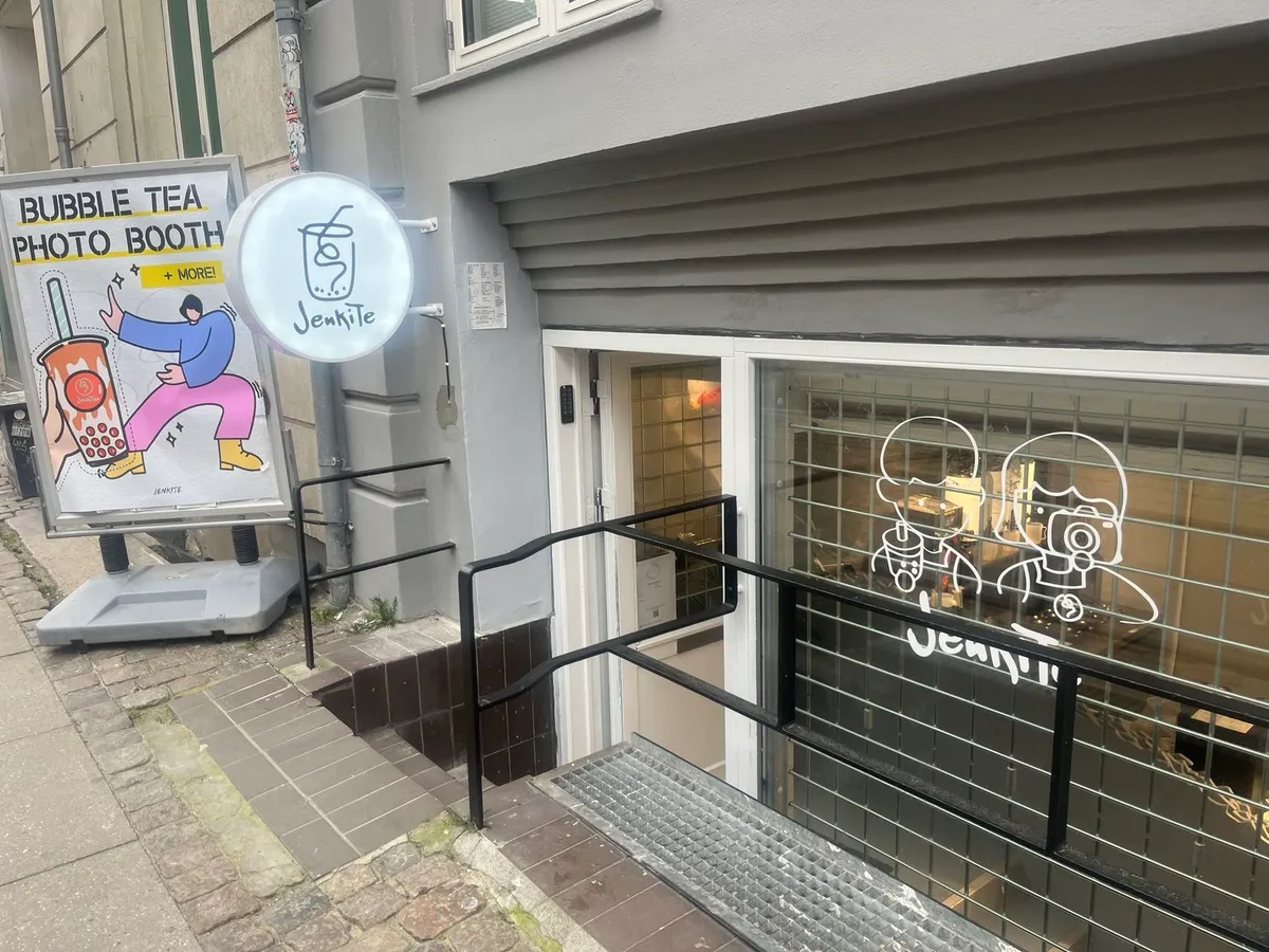 Bubble Tea Shop med Foto Booth og unikt koncept til salg på Vendersgade 10. Foto Booth med karikaturen af to mennesker med kameraer. Stående skilt med illustration af en person med drikke med halm.