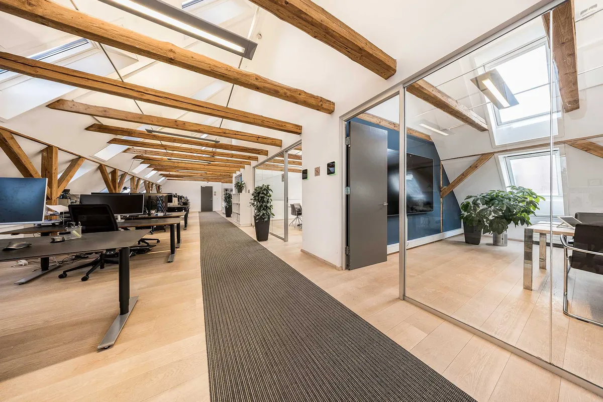 Kontorlejemål med lyse loftsbjælker og glasvægge, moderne møbler og plantearrangementer, lys og luftig atmosfære