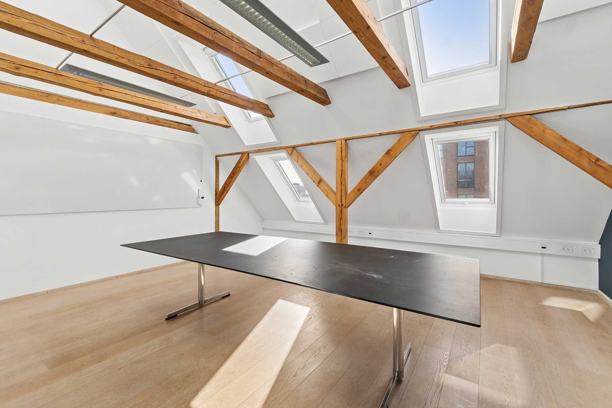 Kontorlokaler med massivt træloft, store vinduer, solrigt og åbent gulv. Moderne mødesal med langt bord og tavle.