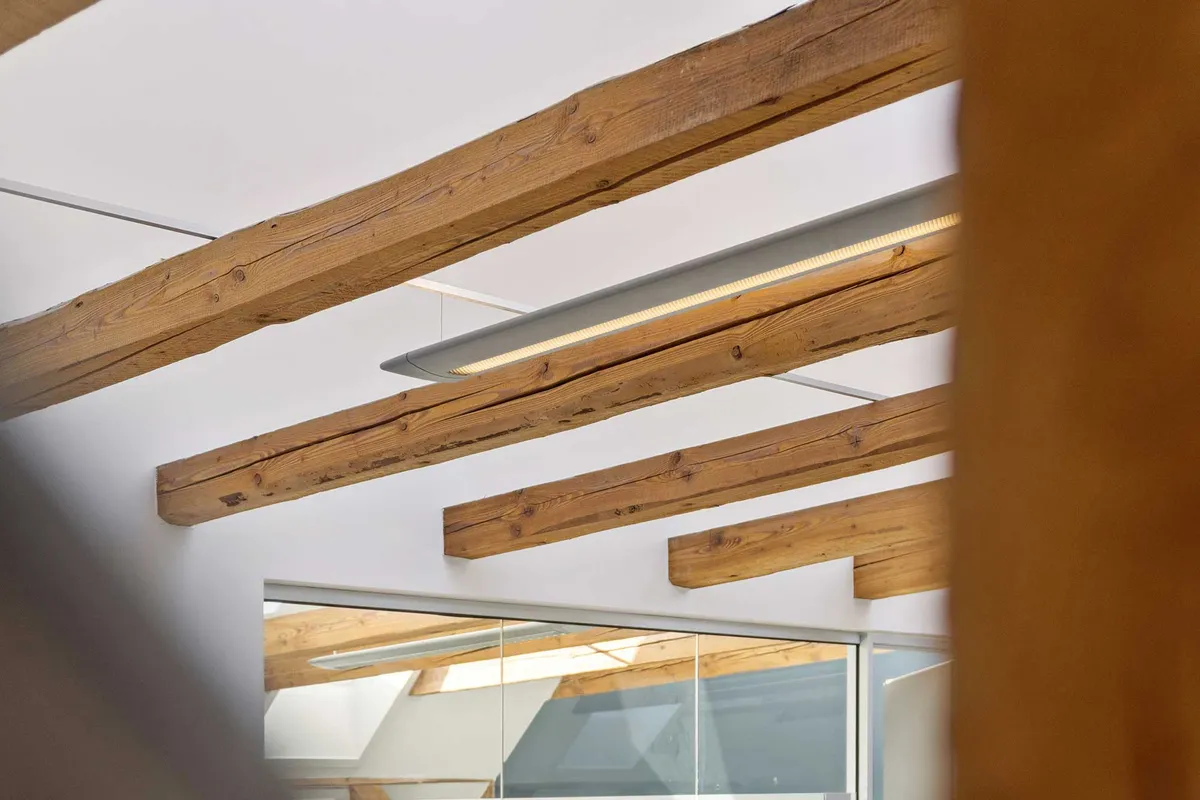 Kontorloft med lyse træbjælker og hængende lysekroner. Loftet er stribet med lyse træbjælker. Loftet er lyst og åbent med store vinduer og hængende lysekroner.