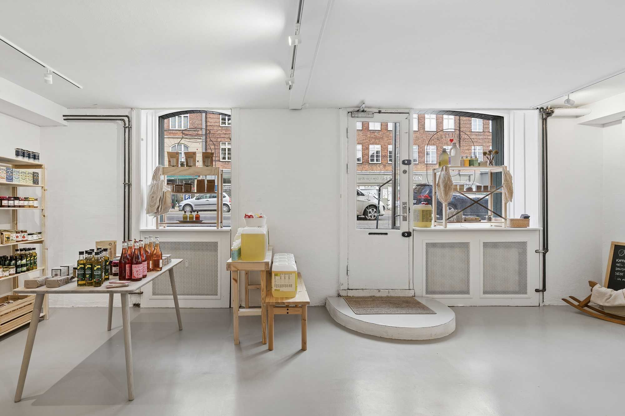 Køkkenbord med flasker og beholdere og en vindue med udsigt til gadebilten og biler parkeret udenfor.