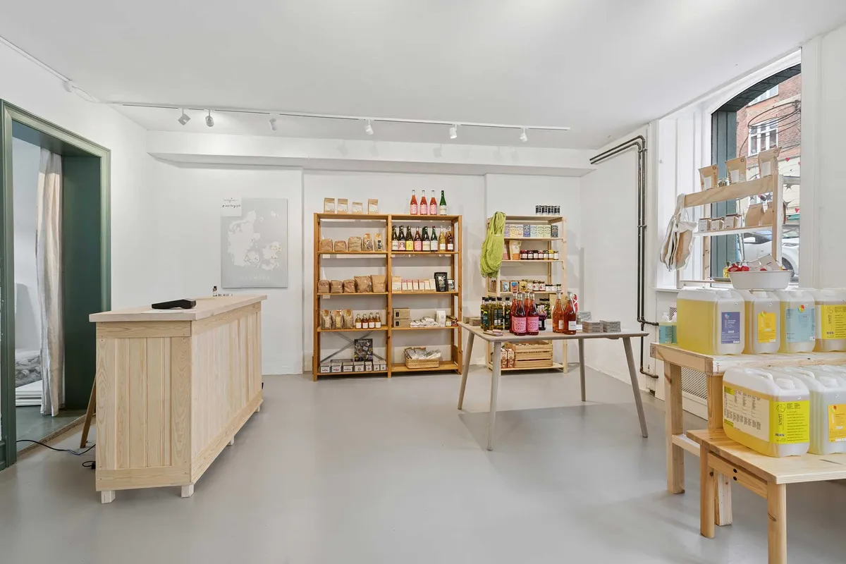 Moderne lejlighedsindretning med lyse vægge, trægulv, simpel møbleret kontorfællesskab med hylder og vinduer