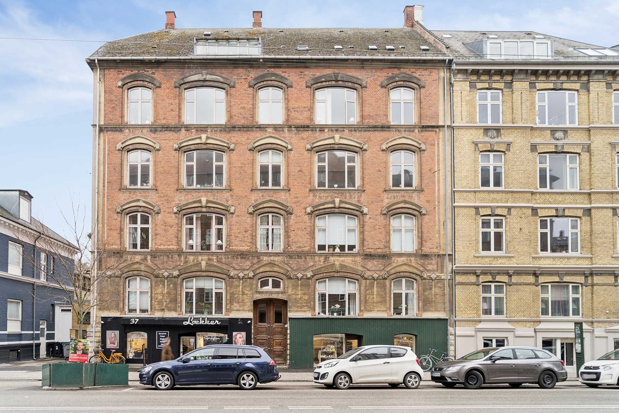 Lejemål i ældre bygning med tre biler parkeret, en skovet og et skilt med Lekker