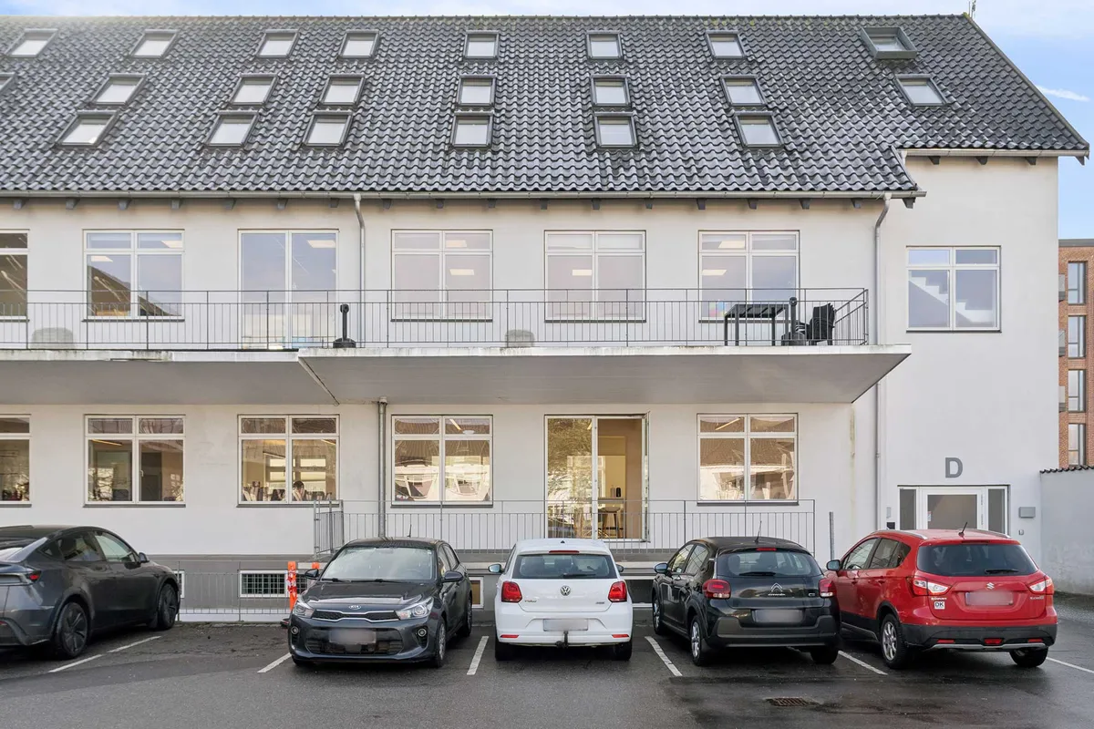 Stilfuldt kontorlejemål med terrasse og vinduer, fem biler parkeret og stol og bord på terrassen