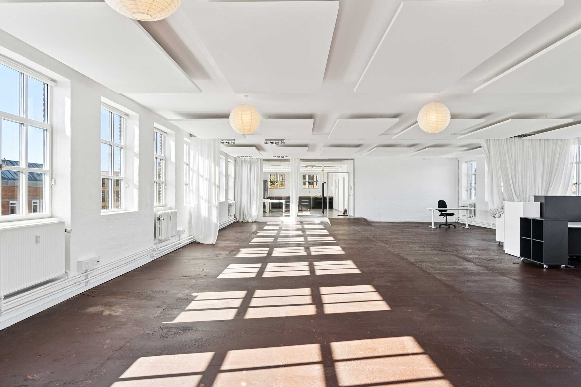 En rå kontorlokal med hvide vægge og loft, store vinduer og massivt lysindfald, hvilket skaber en storslået atmosfære
