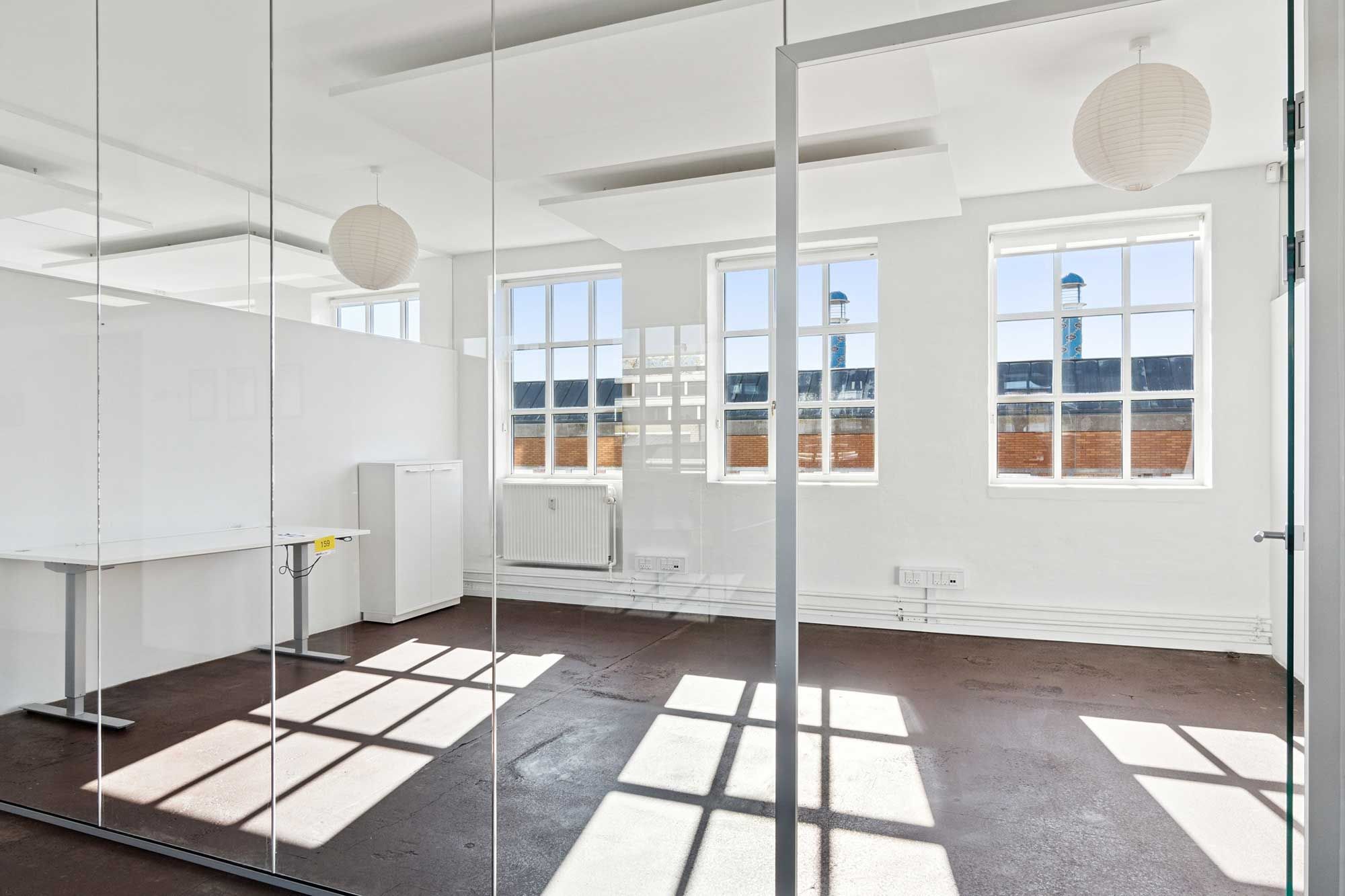 Moderne kontorlokaler med højt loft og lyse, vidvinklede vinduer. Glasvægge og højloftede rum skaber lys og åben følelse. Loftsvinduer giver masser af naturlys.