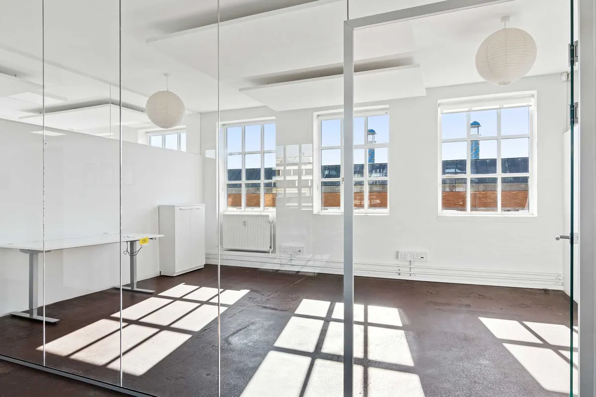 Moderne kontorlokaler med højt loft og lyse, vidvinklede vinduer. Glasvægge og højloftede rum skaber lys og åben følelse. Loftsvinduer giver masser af naturlys.