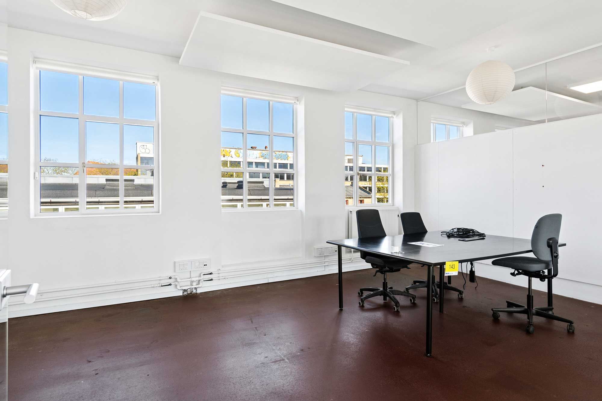 Et tomt kontorlokal med massivt lysindfald og fire kontorstolar. Gulvet er af industritype og der er flere store vinduer