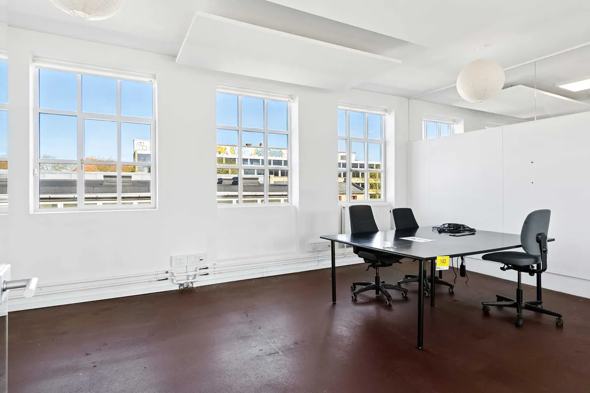 Et tomt kontorlokal med massivt lysindfald og fire kontorstolar. Gulvet er af industritype og der er flere store vinduer