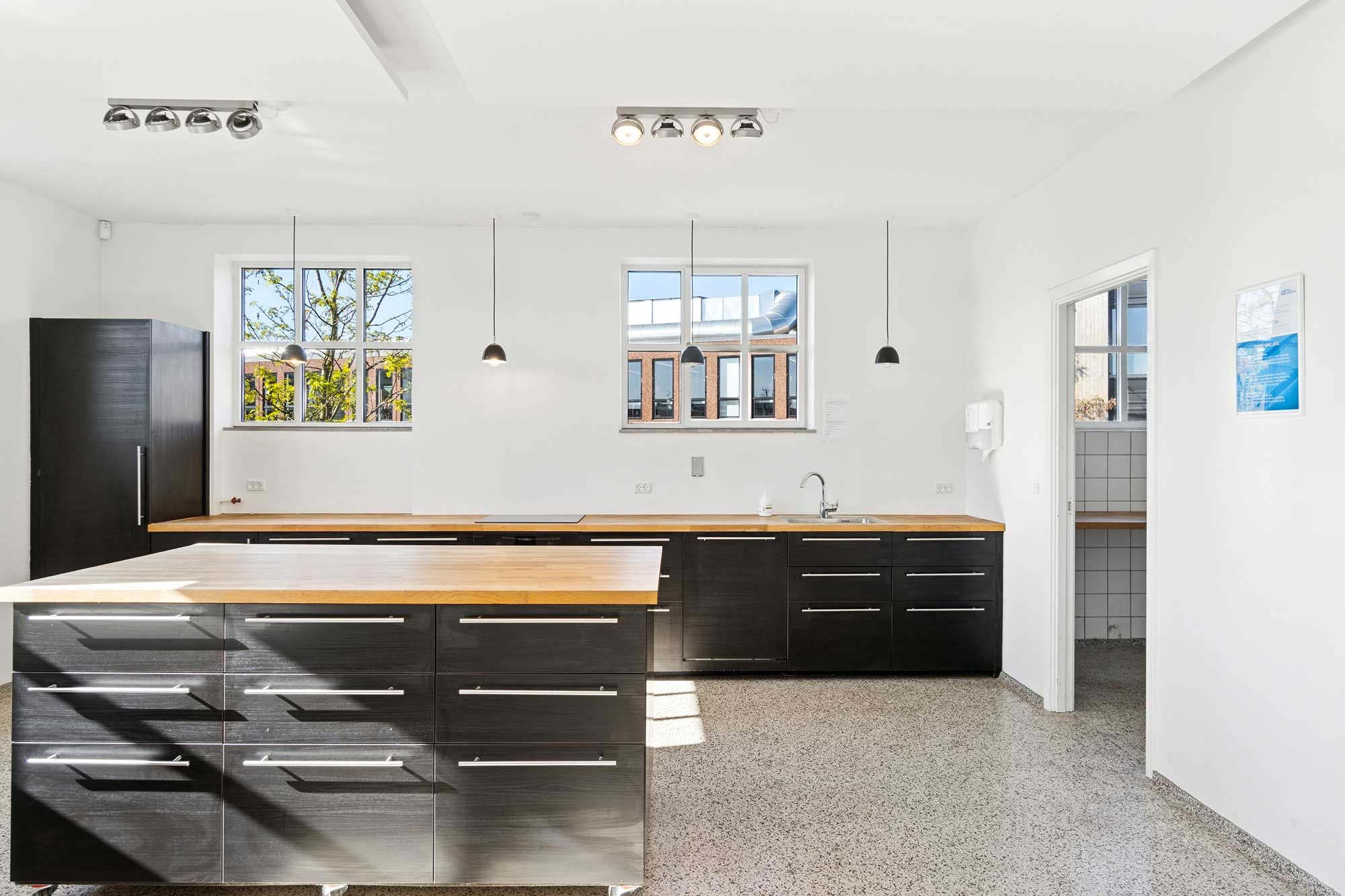 Rå kontorlejemål med lyse loftsvinduer, massivt lysindfald og oprindeligt industrigulv. Slanke møbler og moderne lysekroner.