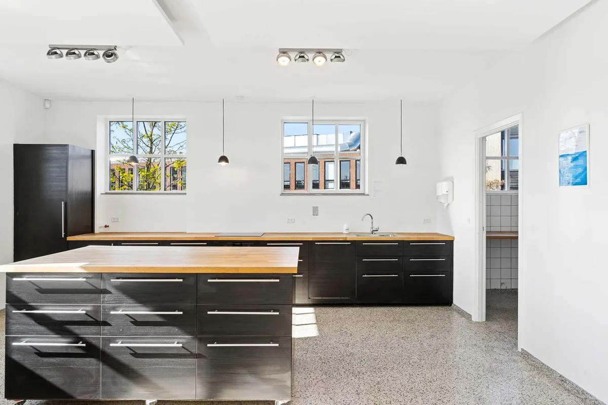 Rå kontorlejemål med lyse loftsvinduer, massivt lysindfald og oprindeligt industrigulv. Slanke møbler og moderne lysekroner.