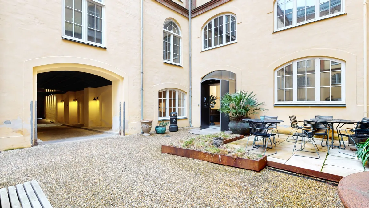 Kontorgård med terrasse, bord og stole, lyse panteoner, grønne planter og urtehave, gul gulv, lyse vægge, moderne møbler, lyse vinduer og lysekroner