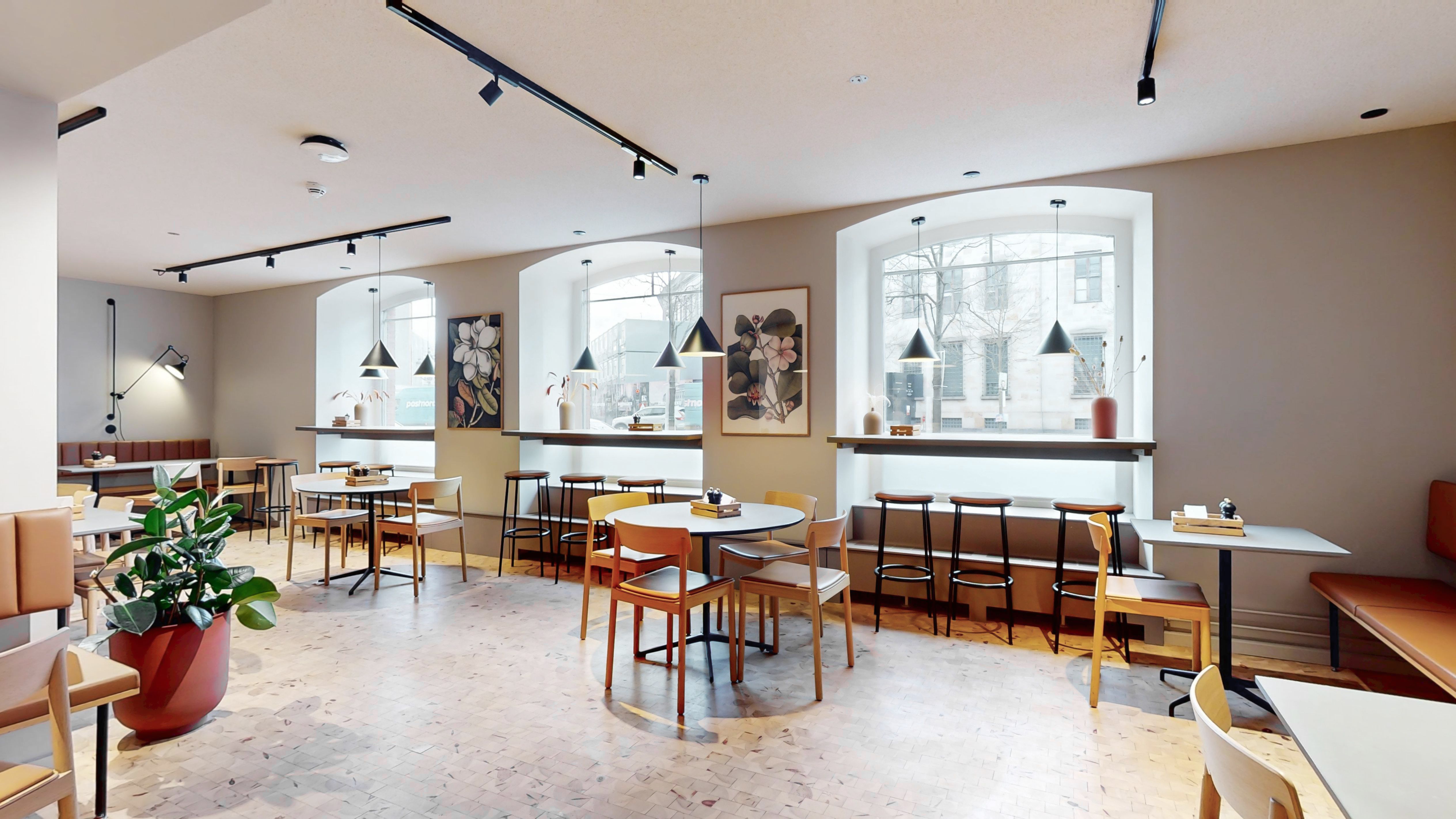 Kontor i baghus med lyse gulve, møbler og vinduer på Holmens Kanal. Lyse loftslampe og små plantepotter.