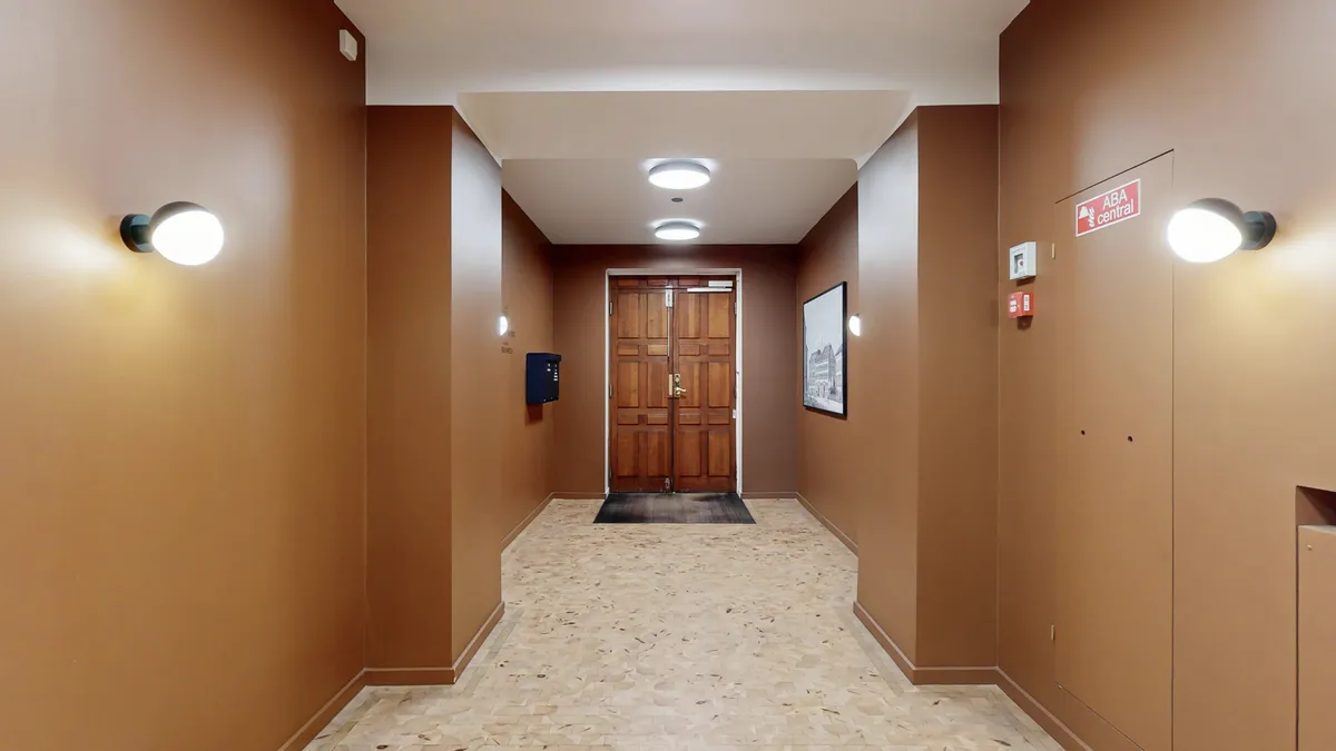 Kontor med marmorgulv og moderne loftslampe. Foto med lysebrune vægge og indgang til lokaler. Plakater med tekst og afstandsmålere på væggen.