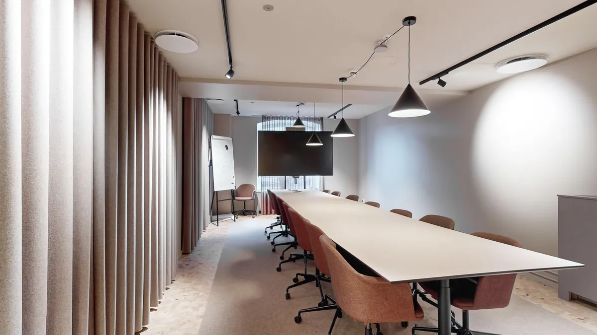 Kontor med bord og stole. Lampetræ med fire lysekroner. Hvid tavle. Gulv og vægge er hvide. Gulvet er tegnet i mønstre.