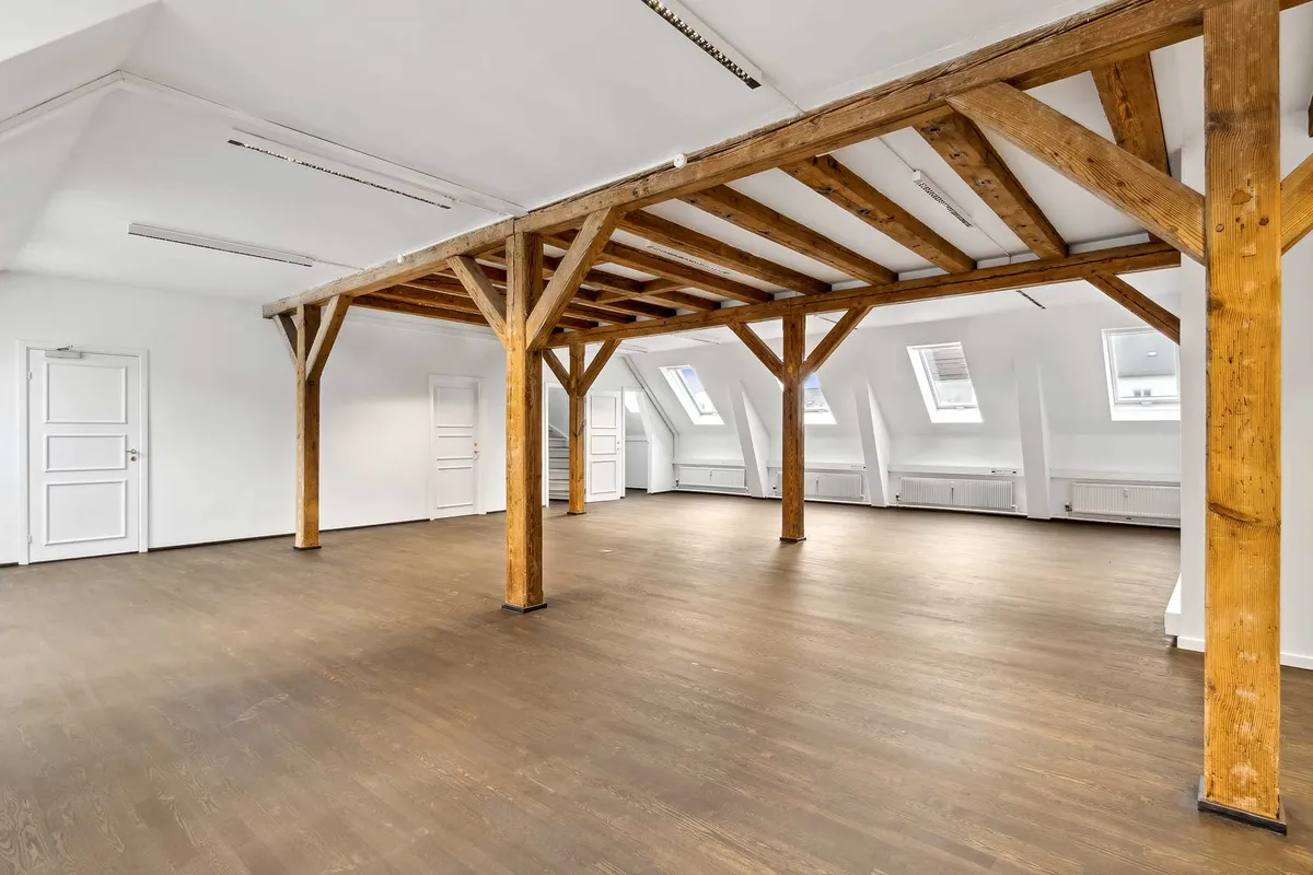 Kontorlokaler med træbjælker og lysegulve, højt til loftet, vinduer og hvide vægge. Sted: Toldbodgade 12, 3., København K