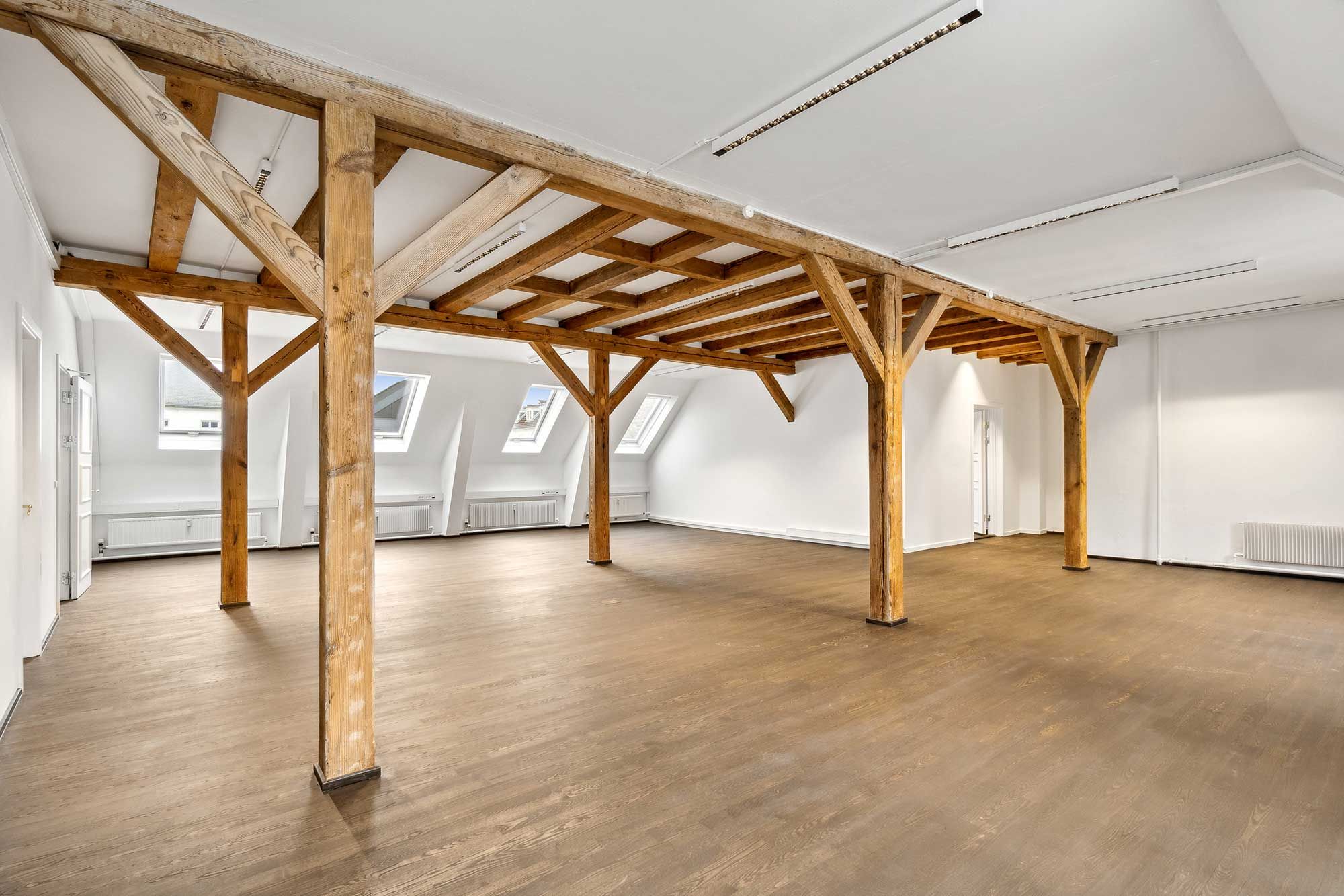 Nyrenoveret kontorlokal i baghuset med højt loft, lyse gulv og træbjælker, hvor vinduer giver udsigt til gaderne og himlen