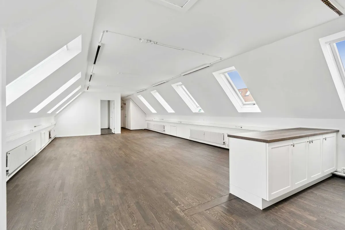 Lukket loft med lyse, højtliggende vindue. Moderne, hvidt møbleret kontorlokal. Højtloftet rum med hårdt trægulv og hvide vægge.