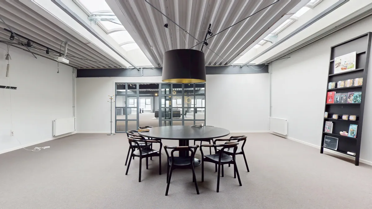 Modernt mødelokale med mørke stole og rundt bord, samt højt loft med lyseruder og loftsbrædder