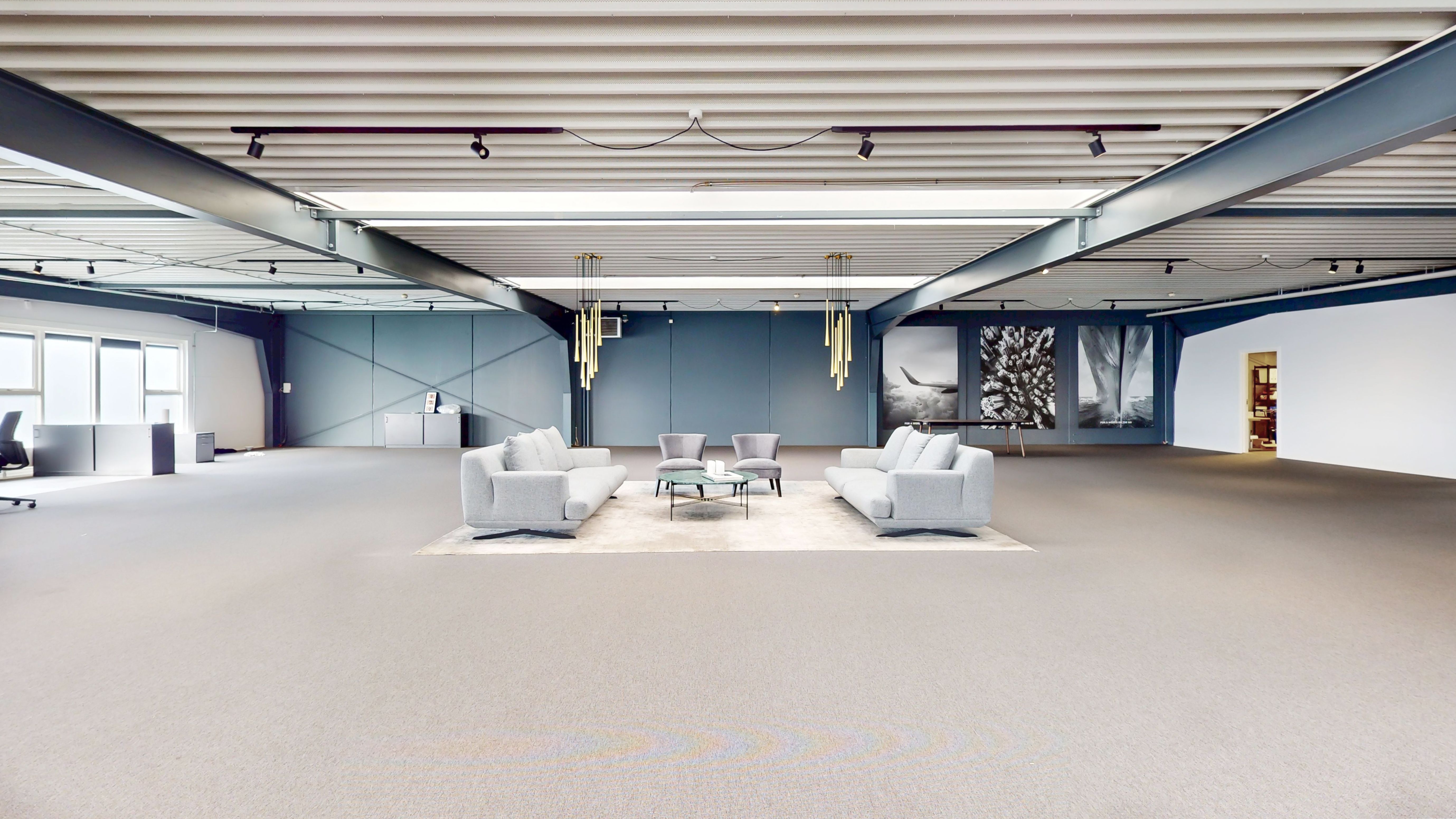 Et stort kontorrum med to sovesofaer, to stole, to kaffeborde, lyse gulvbelægning, gulve og hvide vægge med kunstværk