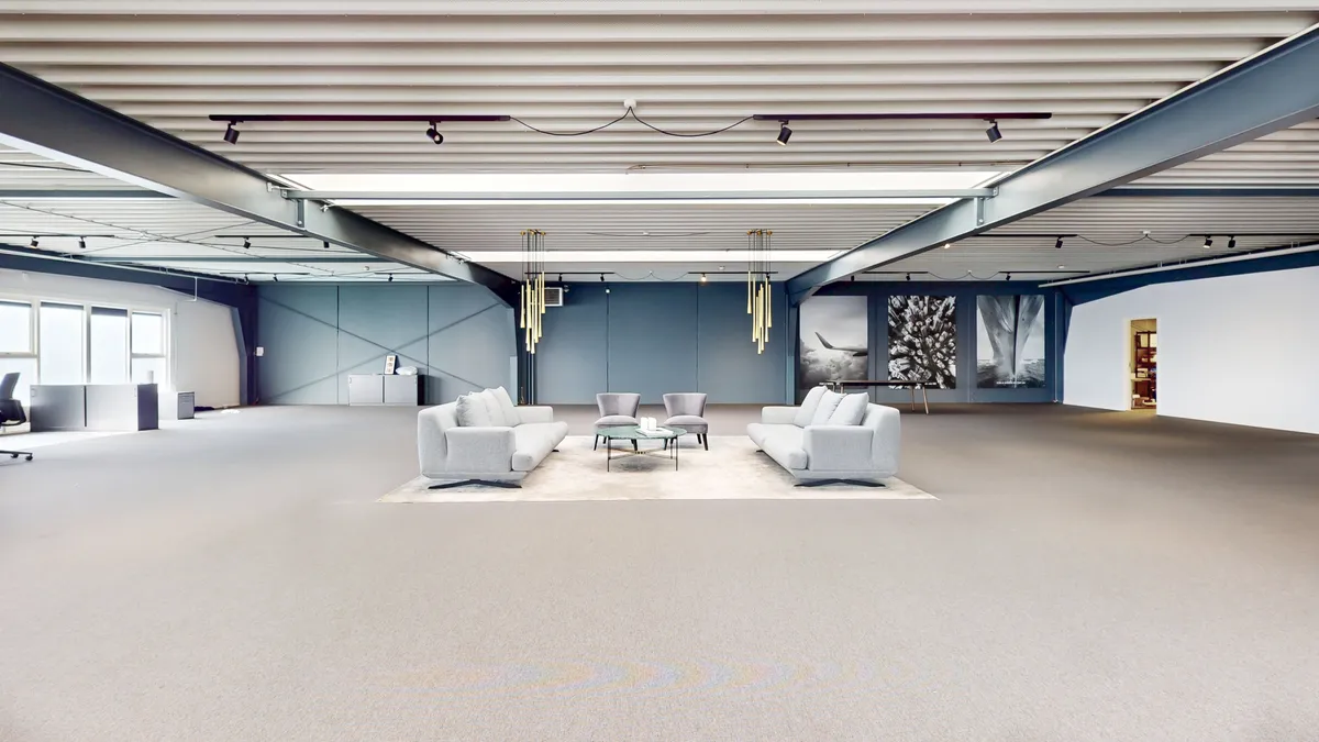 Et stort kontorrum med to sovesofaer, to stole, to kaffeborde, lyse gulvbelægning, gulve og hvide vægge med kunstværk