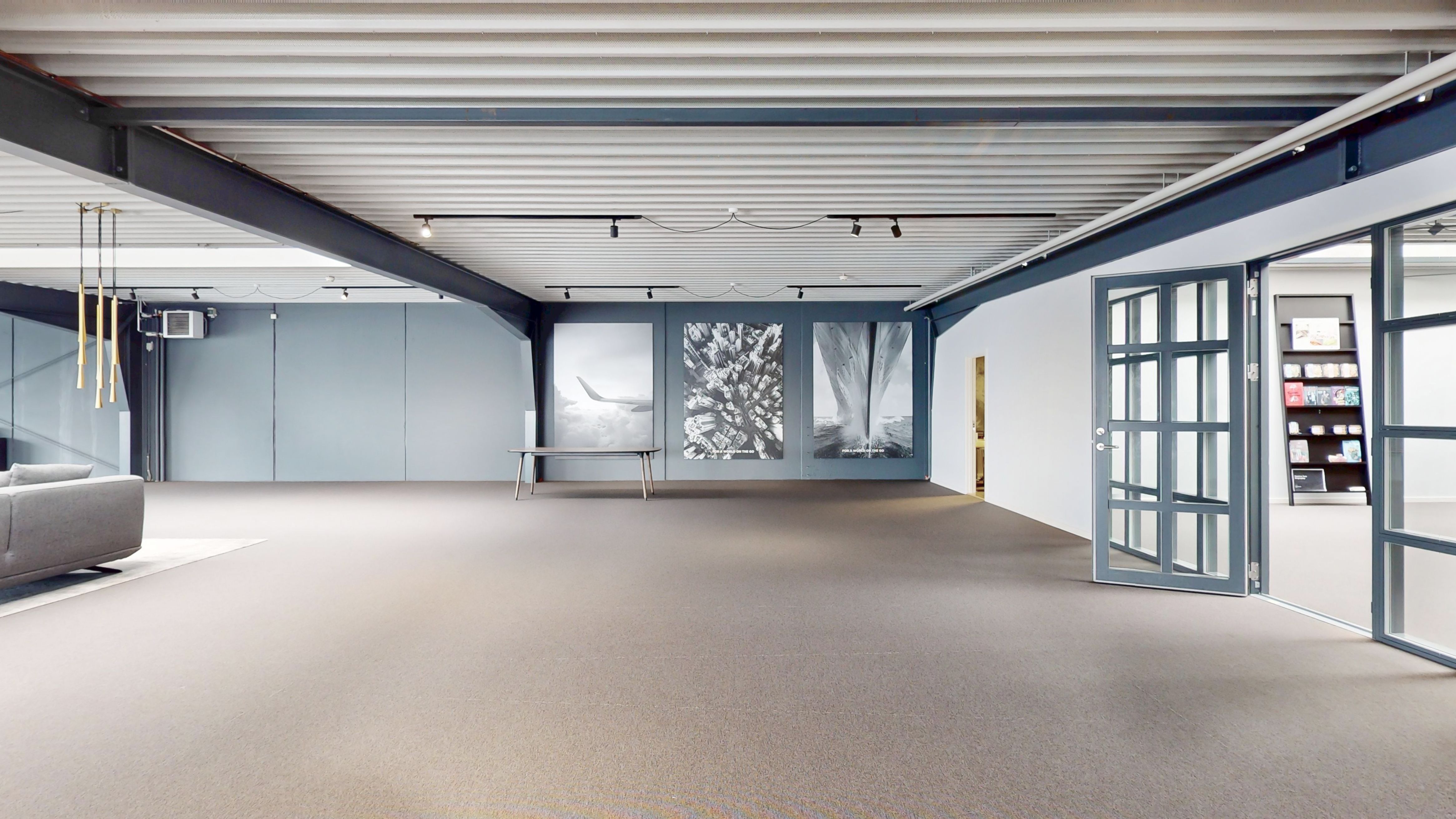 Det store kontor har åbent og fleksibelt gulvplan med lyse lofter og store vinduer. Væggene er lyse og minimalistiske og der er et stort, tomt rum med en stol og lyse gulvbelægning.