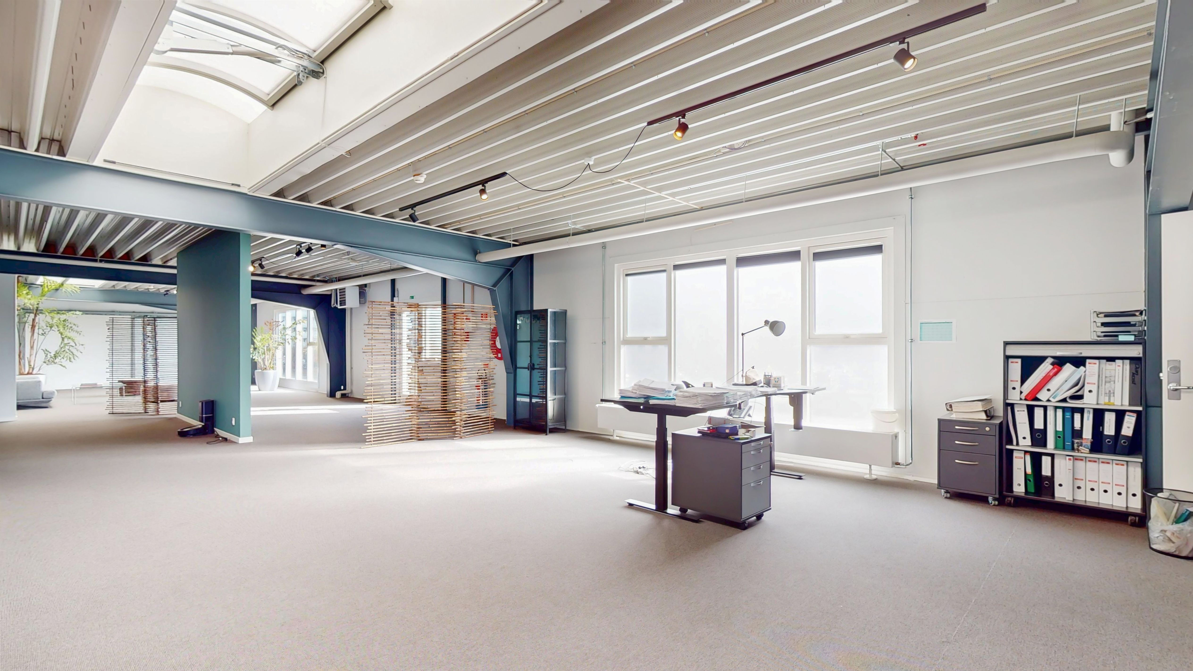 Et stort kontor med højt loft og vinduer, skrivebord og stol, højre side med bøfler og papirer og bibliotek med mapper og filer