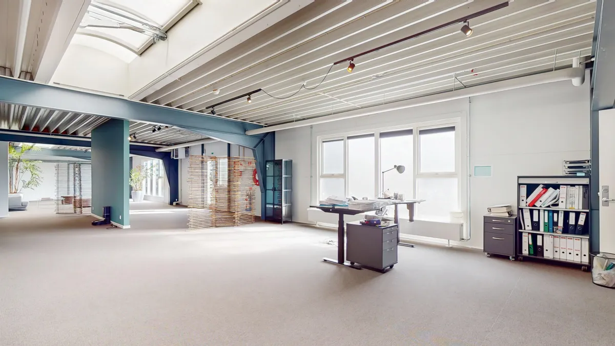 Et stort kontor med højt loft og vinduer, skrivebord og stol, højre side med bøfler og papirer og bibliotek med mapper og filer