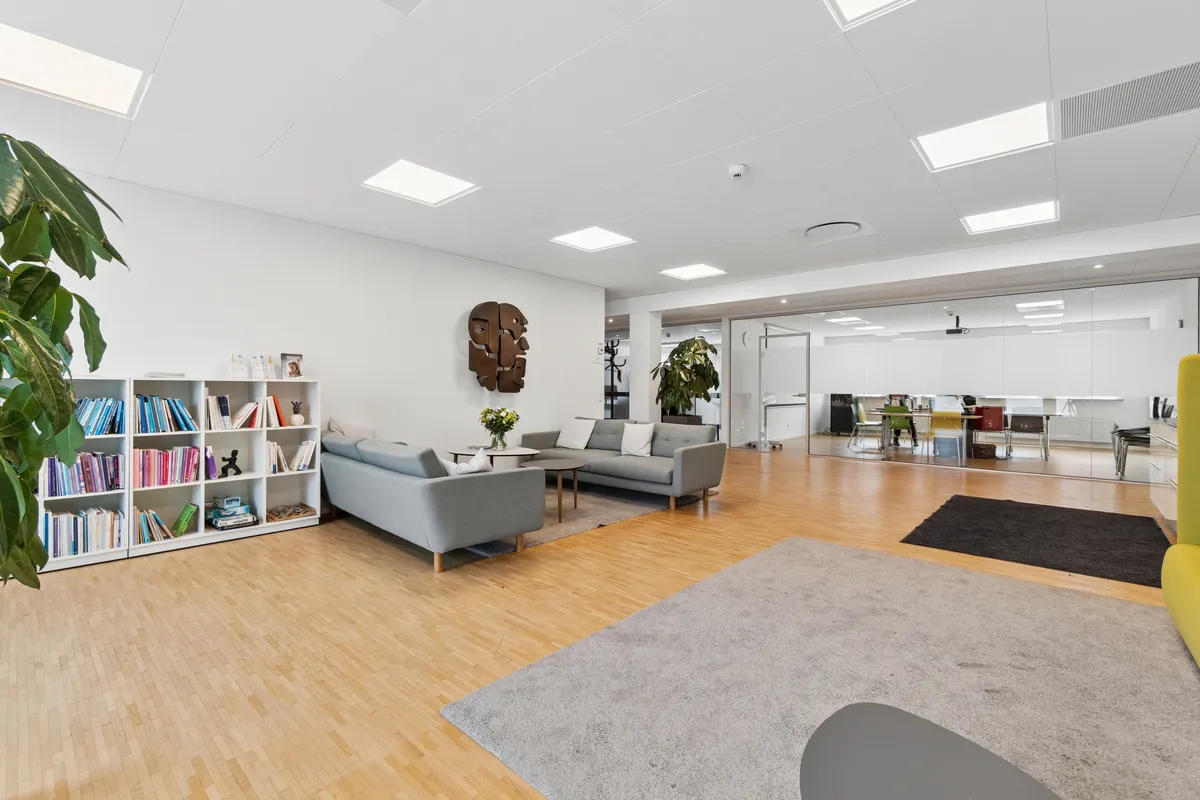 Kontorlokaler med moderne indretning, hvidt loft, lysegulve og flere møbler samt sofaer, bibliotek og skrivebordsbord