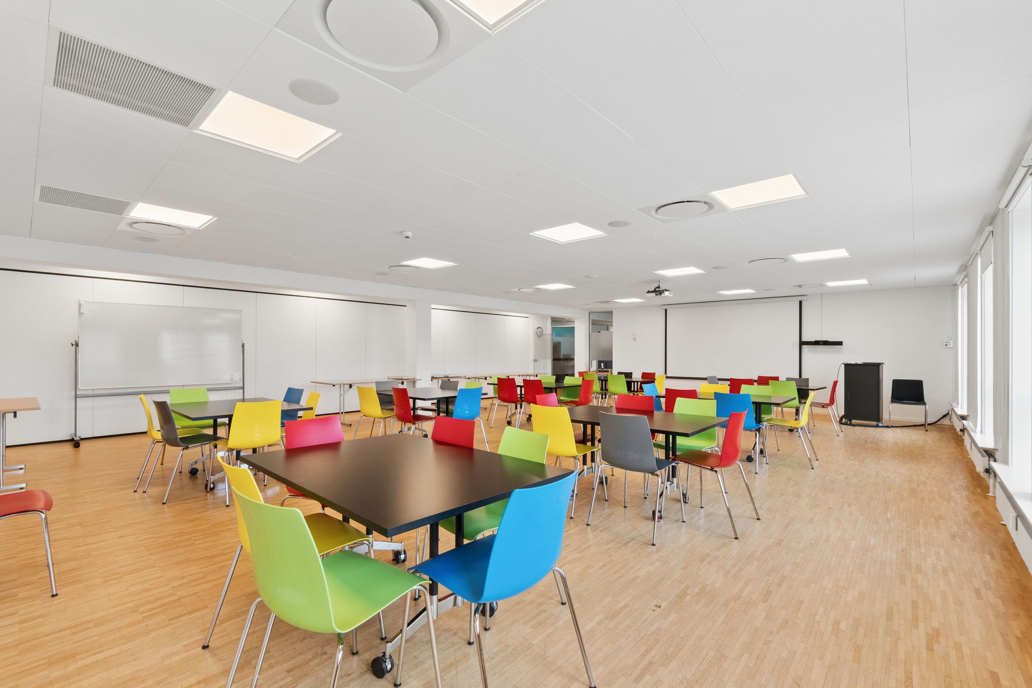 Kontorlokaler med lyse farvede stole og borde placeret i et moderne møbleret rum med højt til loftet og hvide vægge