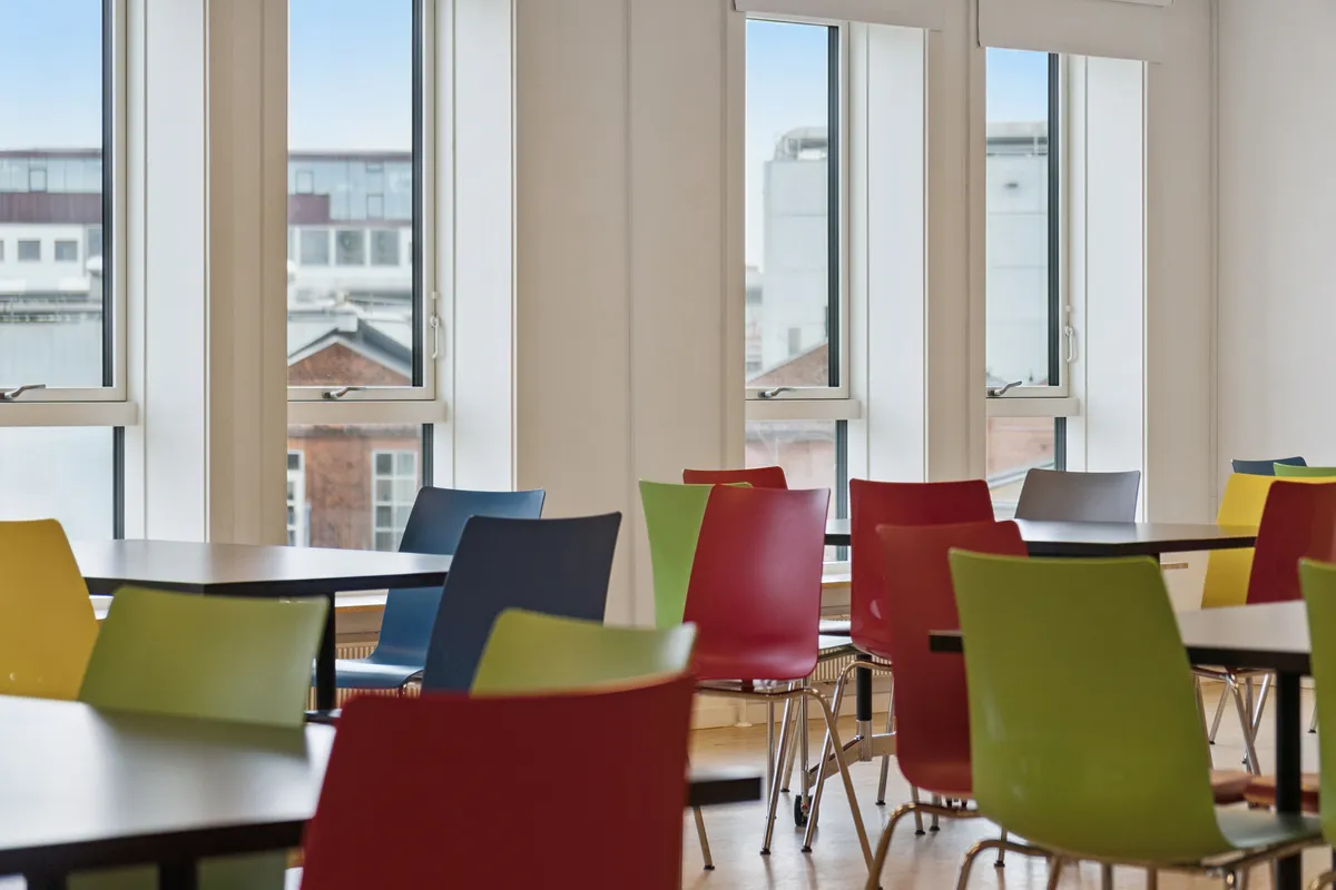 Kontorlokation med mange lyse farvede stole og borde samt store vinduer med udsigt til byen og Nørrebro Station
