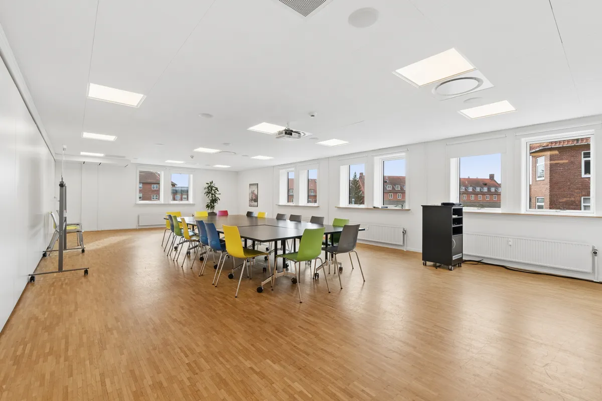 Moderne mødelokale med lys, trægulv, vinduer med udsyn og højtloft. Mødelokale med lyse lofter, projektor, trægulv og lyse, farverige stole
