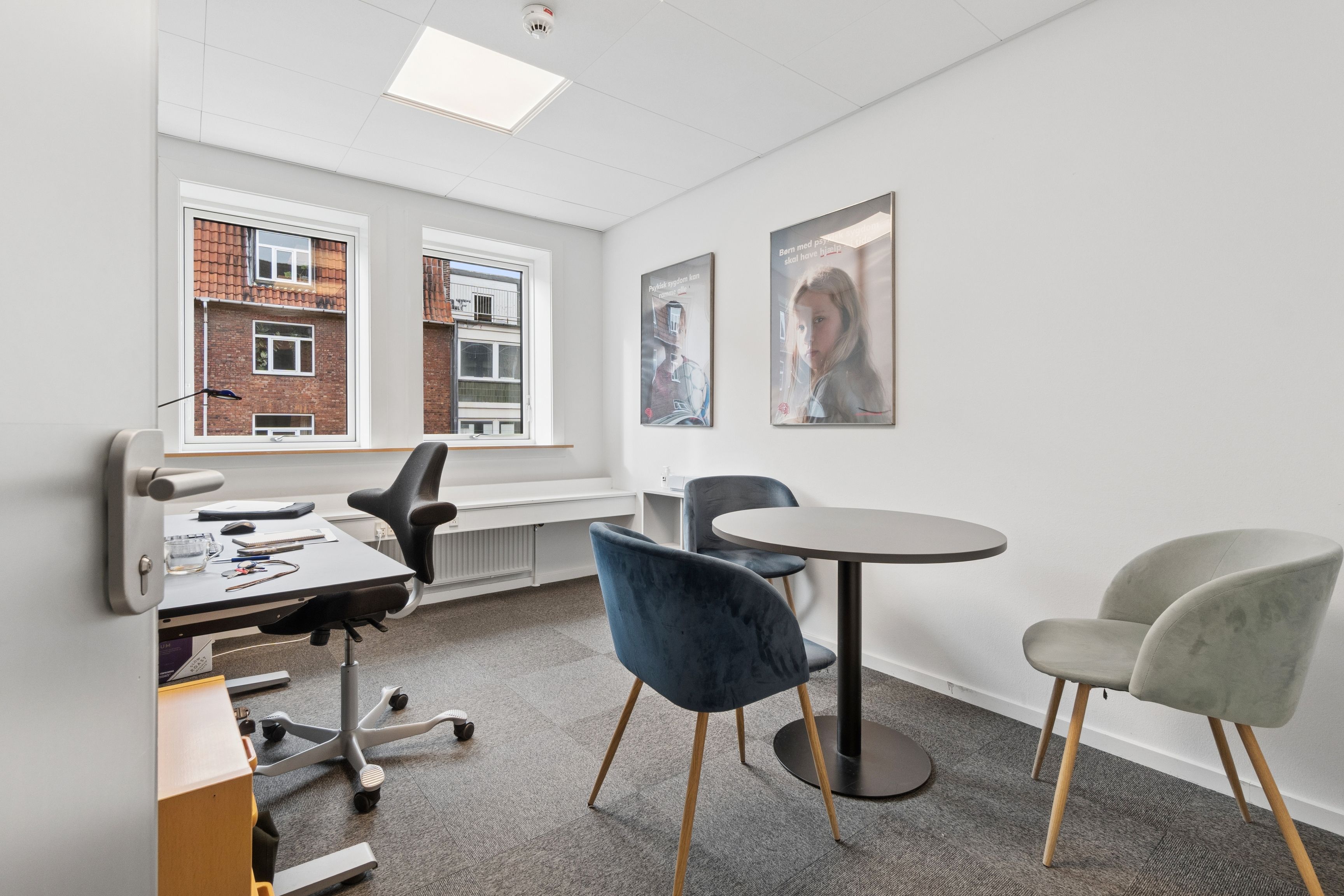 Kontorrum med moderne møbler og lyse vinduer, tavle, bord og fire lænestol, indretning med fire poster og fire plakater på væggen