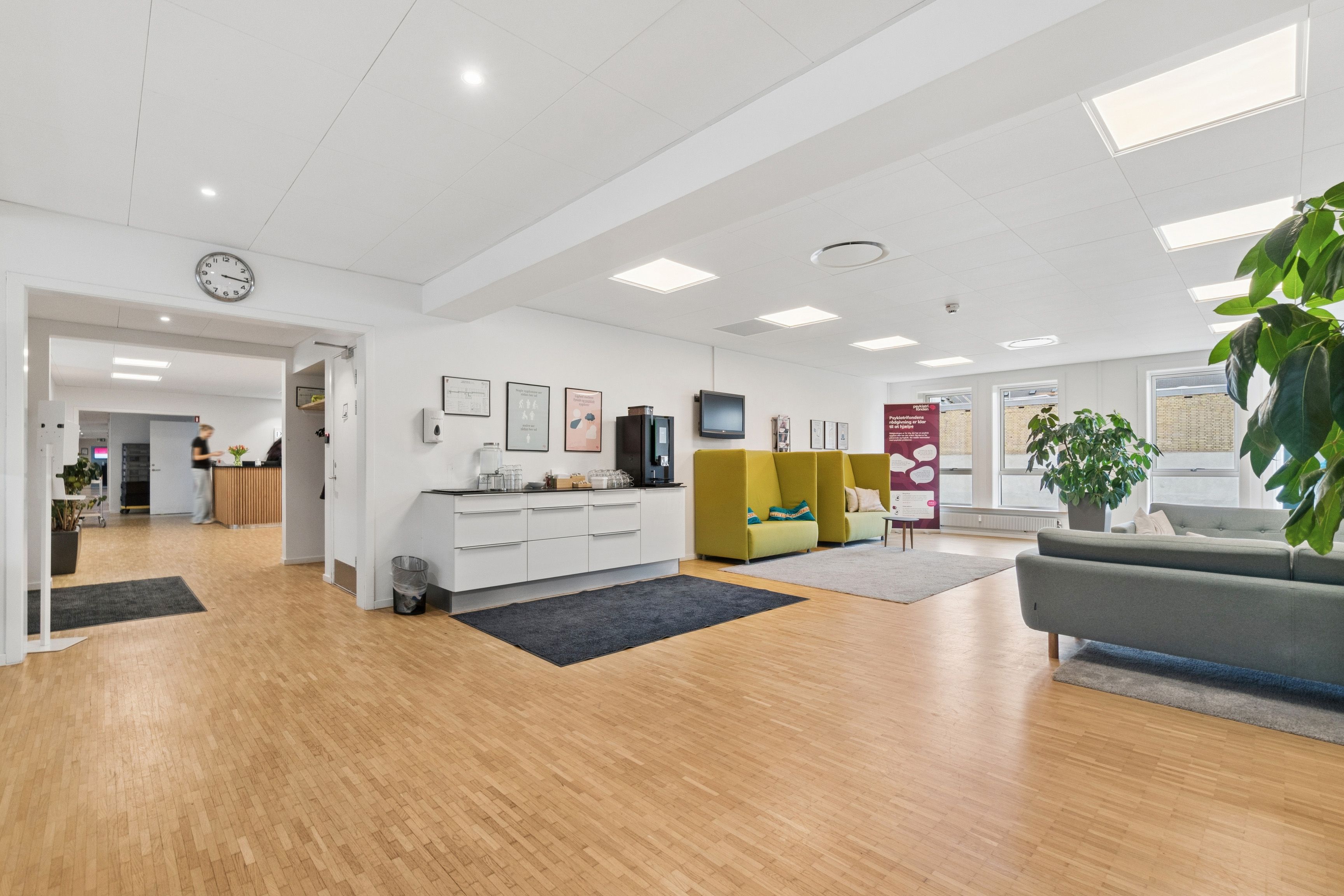 Indbydende kontormiljø med hvidt loft, højt kvalitetsniveau og lyse gulve samt sofaer og plantepotte i rummet