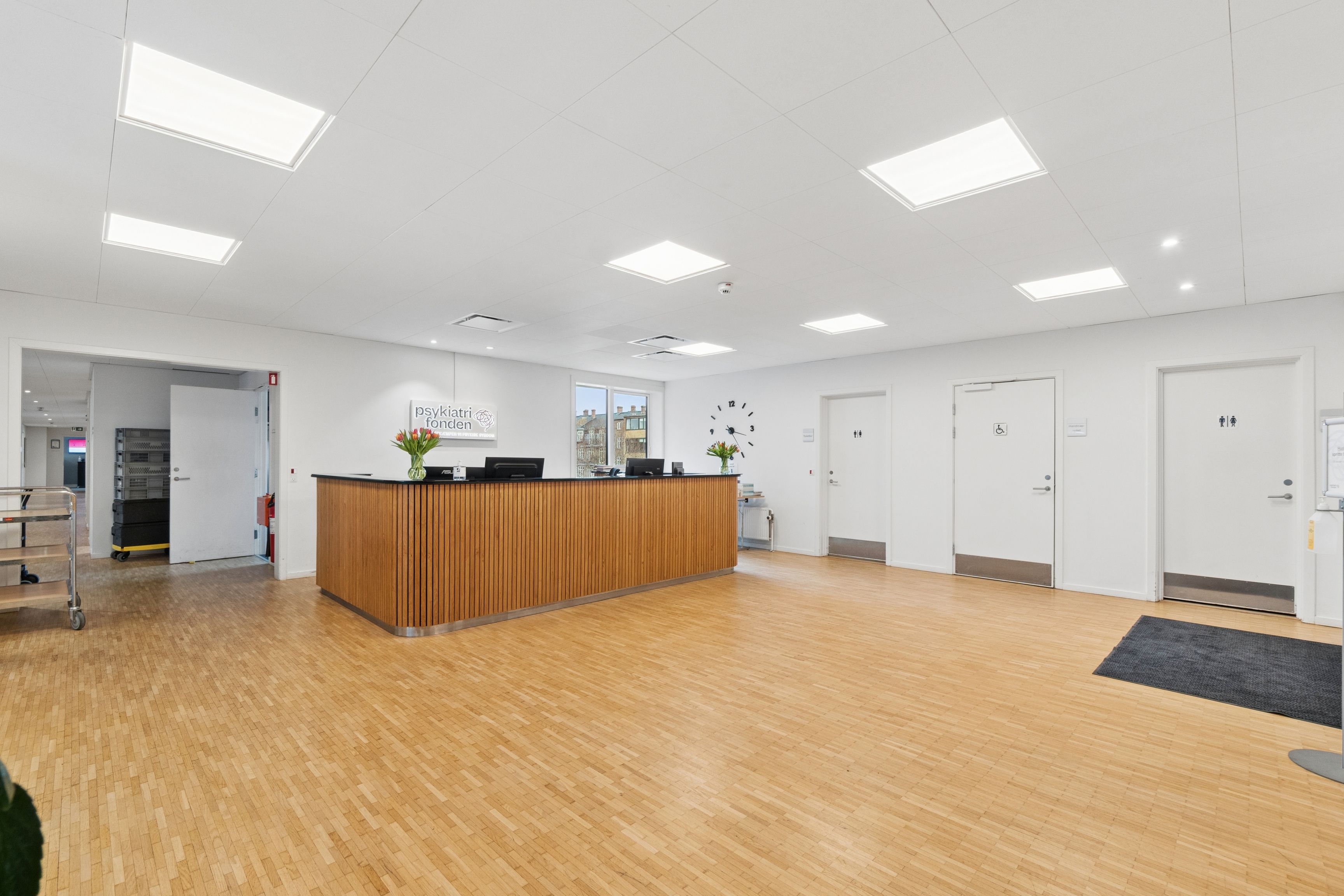 En stor lobby med lyse loftslamper, moderne skrifttyper, en stor bænk og to døre til højre og venstre side af lobbyen