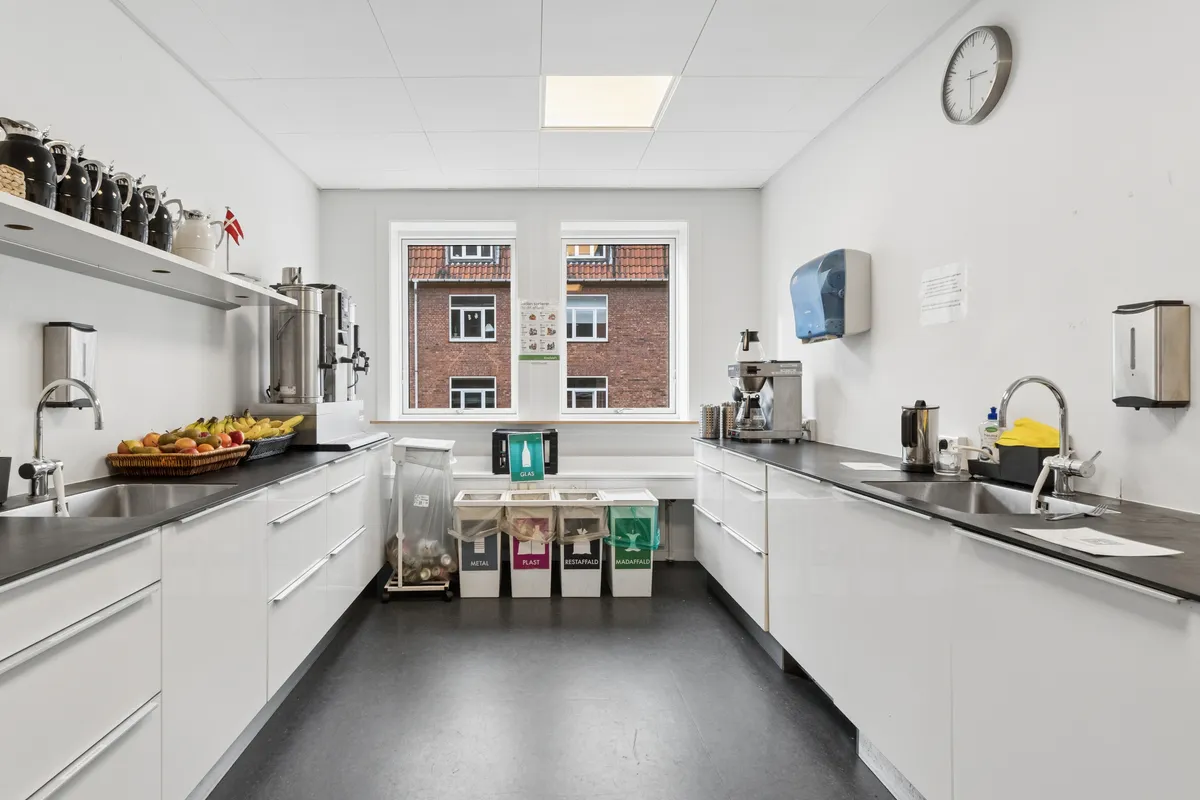 Indkøbskøkken med lyse krydderier, frugtkurv, kaffemaskine og flere skraldspande for forskellige materialer på en hvid belægningsgulv