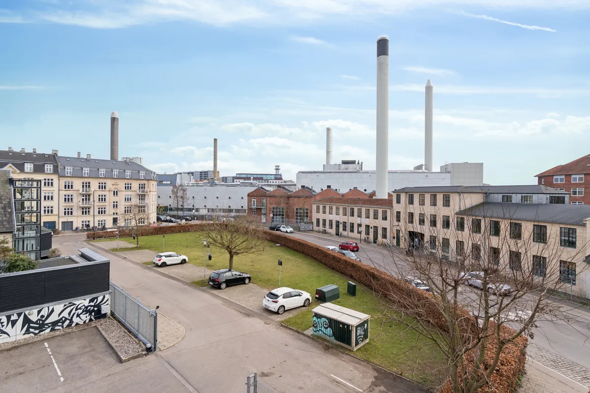 Flyfoto over et kontorområde med parkerede biler og grønne træer, samt flere bygninger med høje røgstove, ligesom der er en grøn parkeringsplads