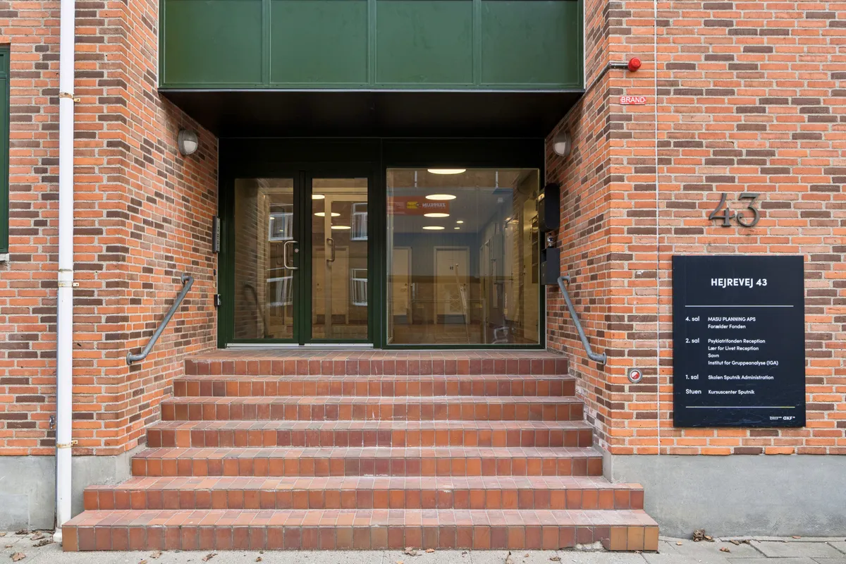 Indgangsparti til Hejrevej 43 med forskellige kontorer, som har lyse glasdøre og vinduer samt rød murstens facade