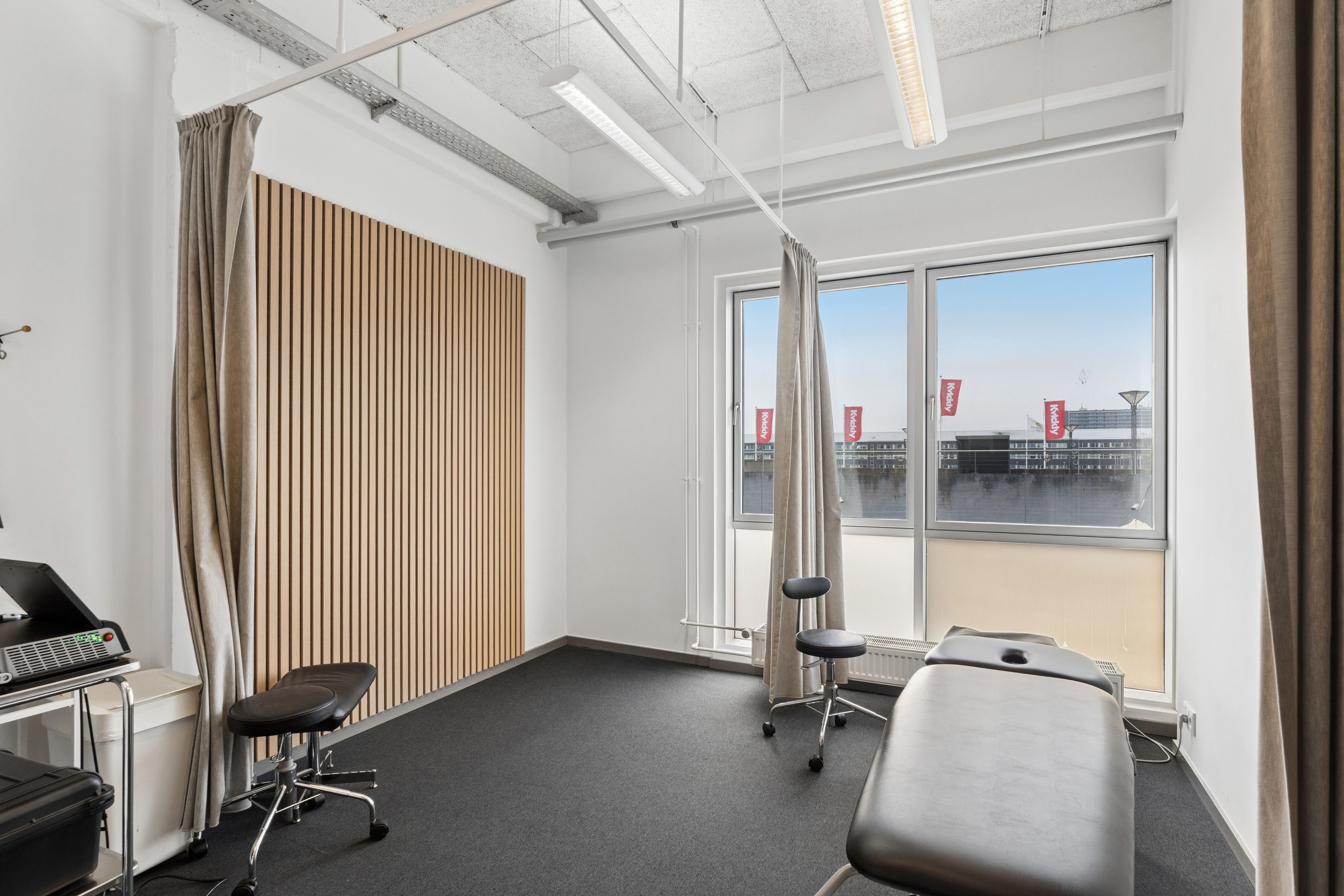 Kontorrum med højt til loftet og store vinduer til leje på Nygårds Plads 21, 1. etage. Rummet indeholder to lægestolar og en massagebord samt teknisk udstyr.
