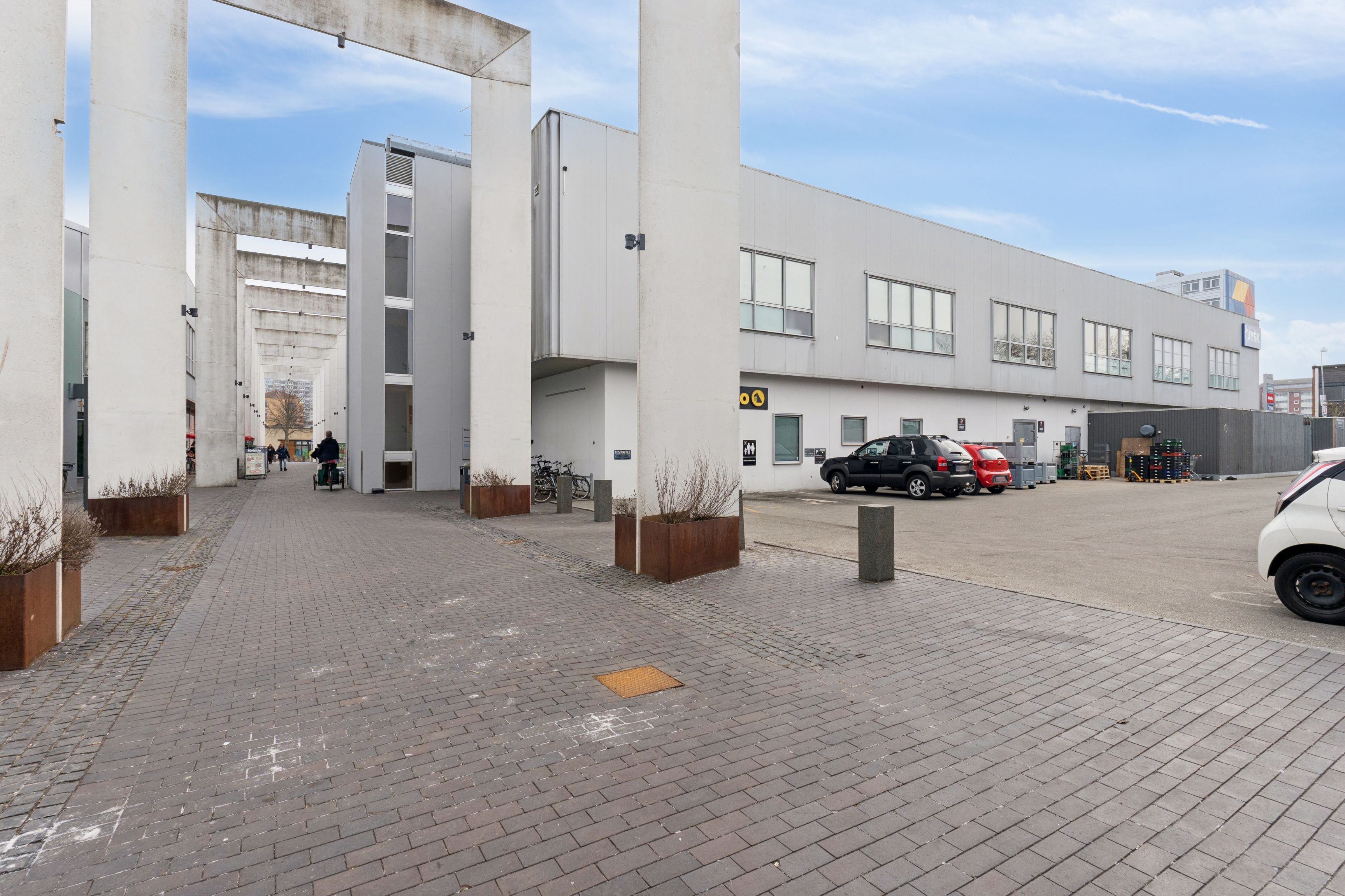 Højbygning med garage til leje i Brøndby med store vinduer og moderne design, samt klippestensgulve og en række parkerede biler