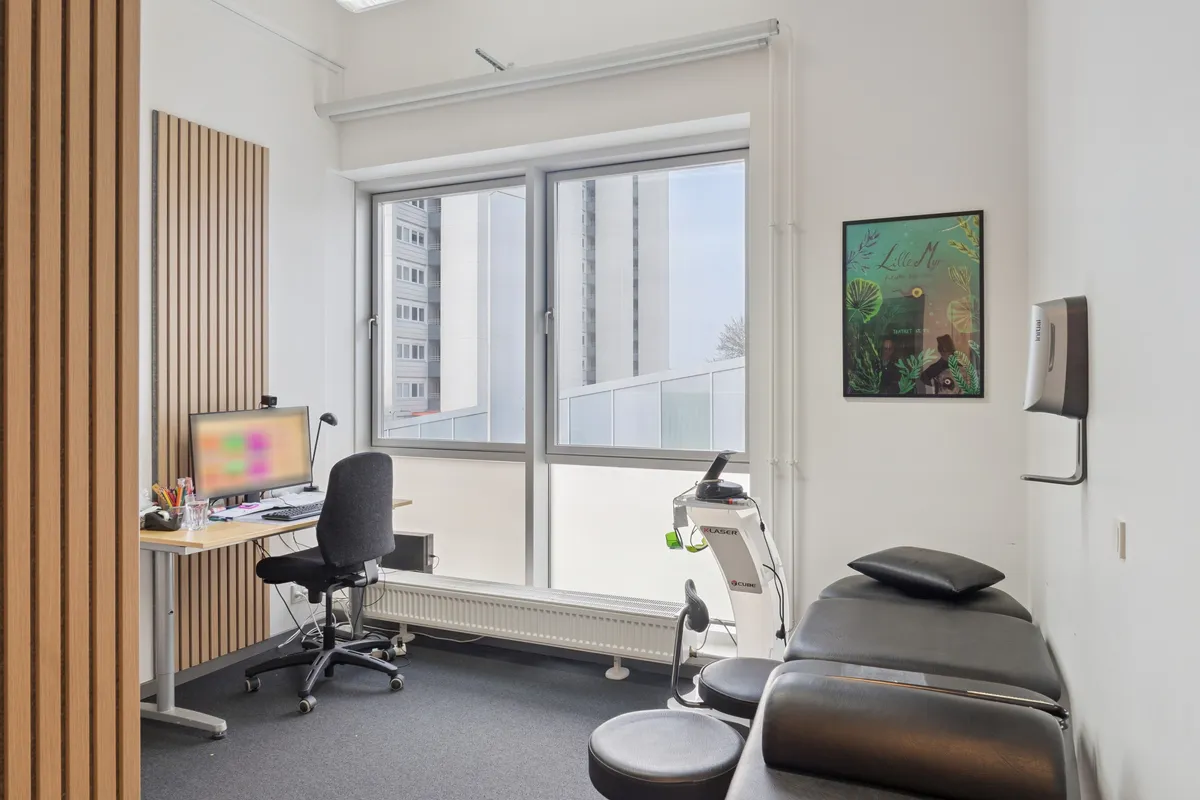 En stor stue med højt til loftet, vinduer, skrivebord med computer, stol, stribet væg og et motionsapparat med sæde