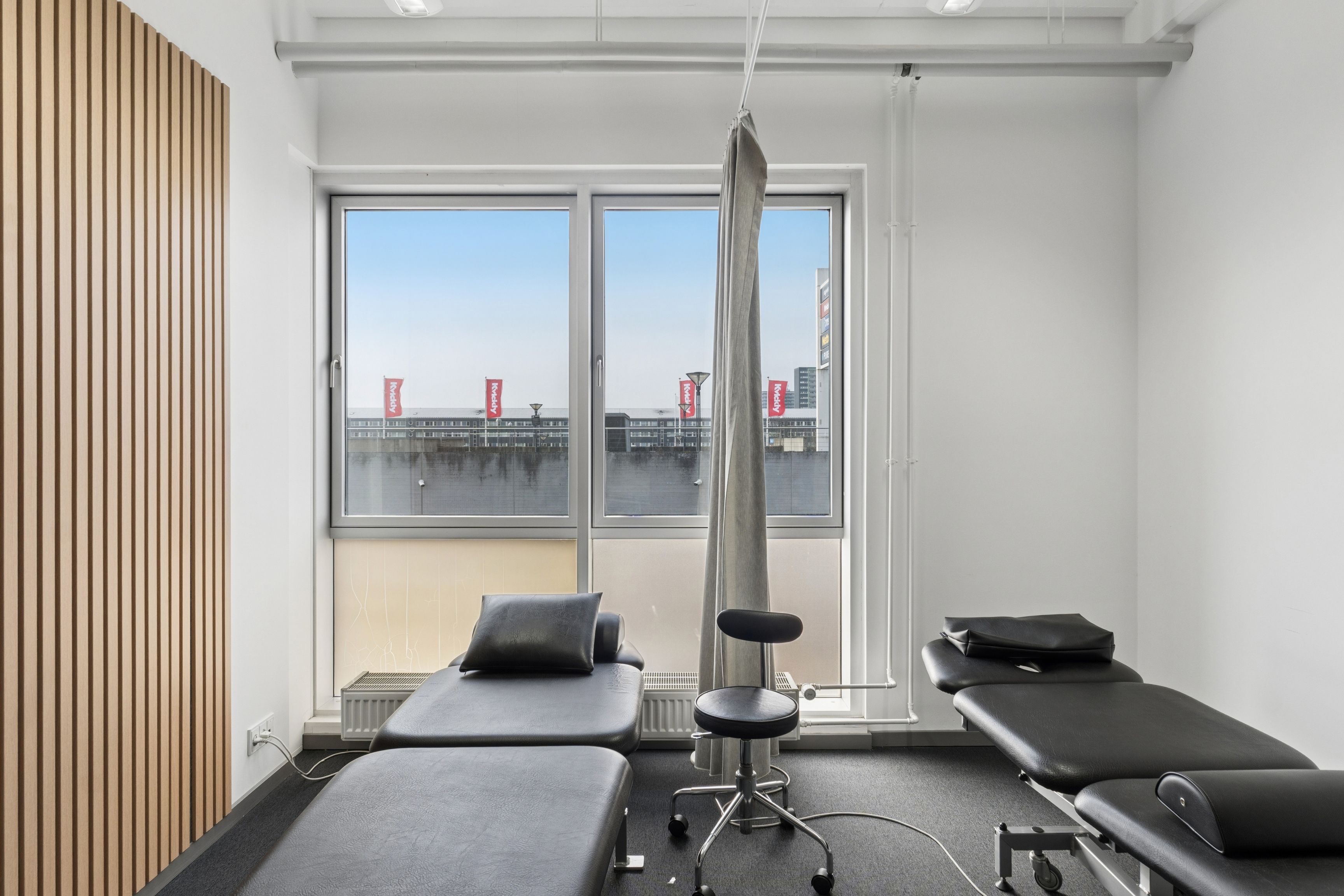 En klinisk arbejdsplads med fire behandlerrum, hvert med en massageseng og en høj, hvid væg og loft