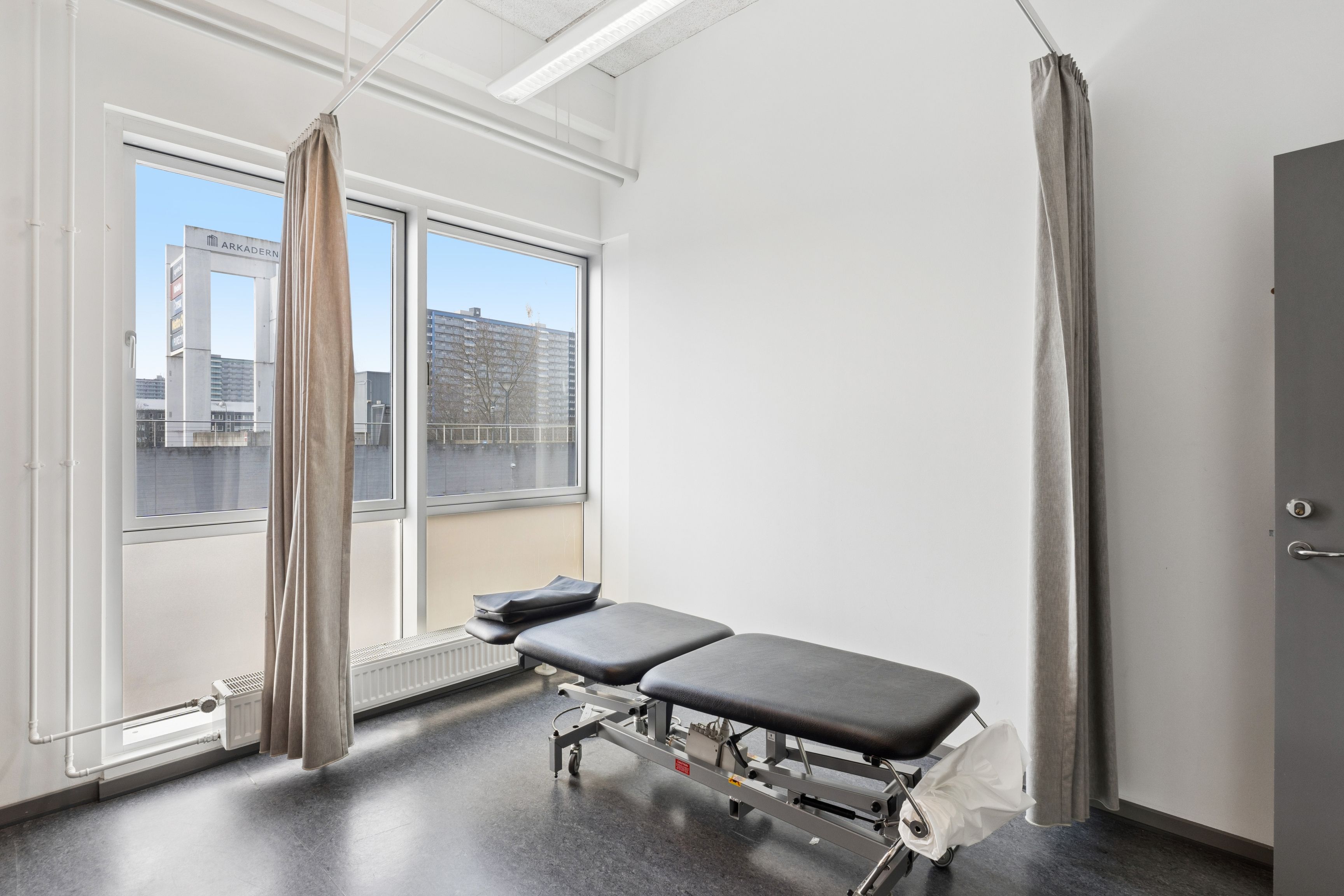 Lejlighed med to lægeborde og højt til loftet med store ruder og lysindfald fra en bygning med skrift over vinduet